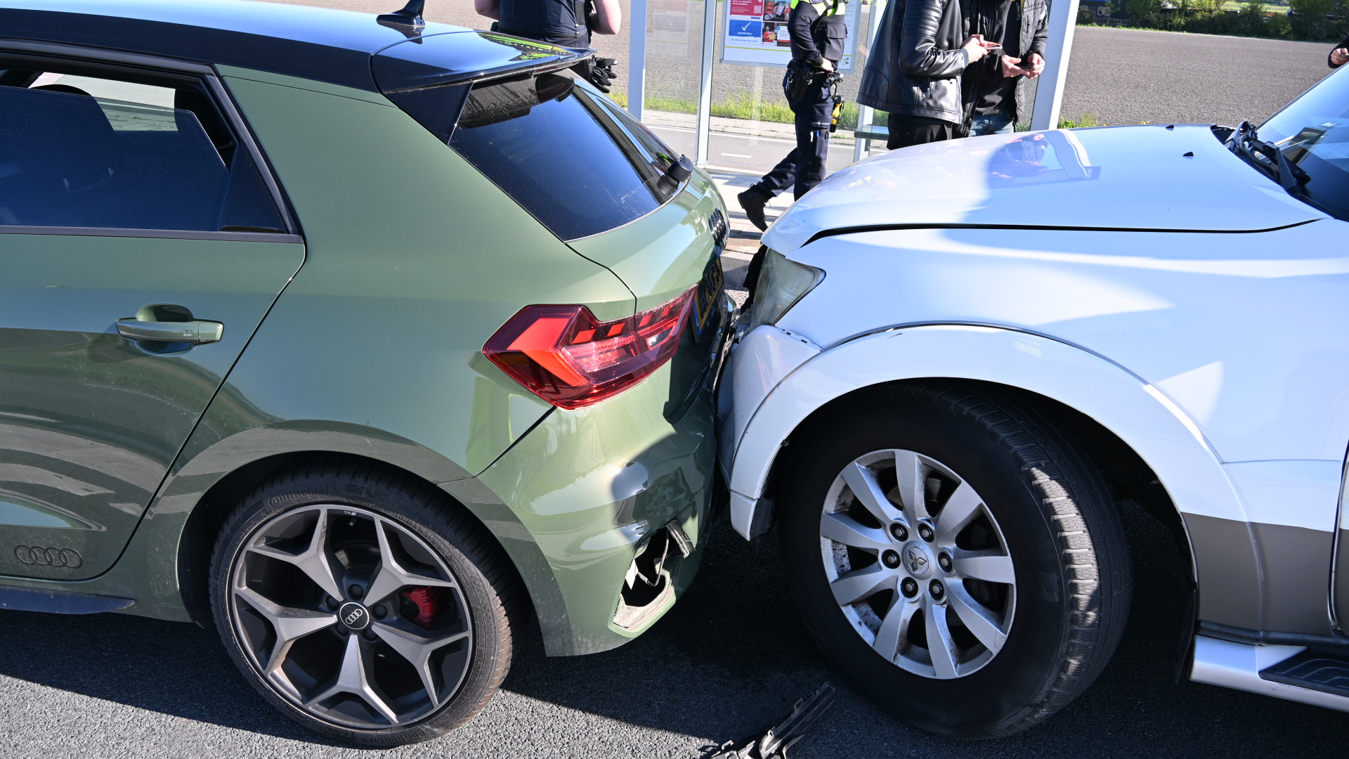 Twee auto's, een groene en een witte, zijn gebotst, met schade aan de achterkant van de groene auto.