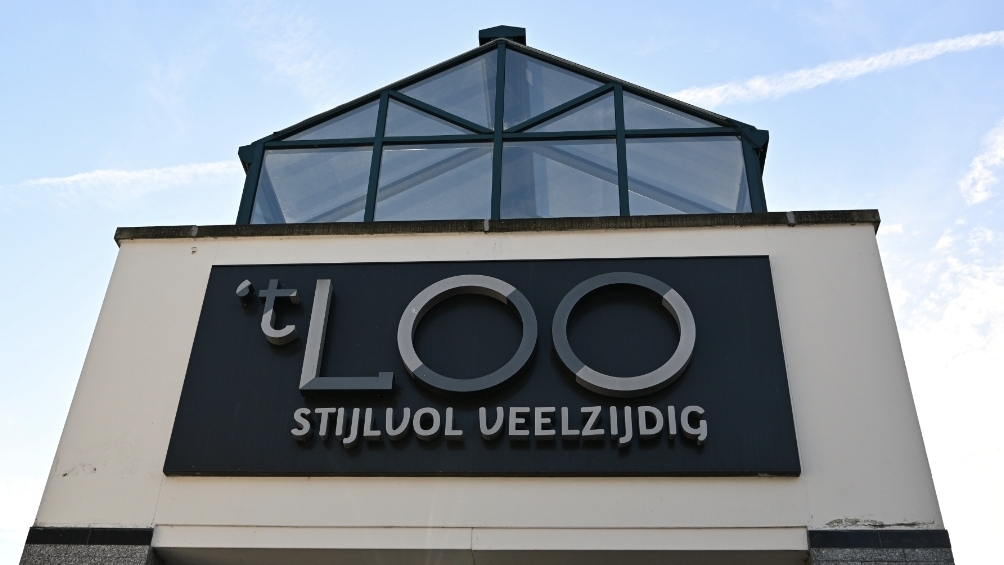 Gevelbord van een gebouw met tekst "'t LOO Stijlvol Veelzijdig" onder een glazen dakconstructie.