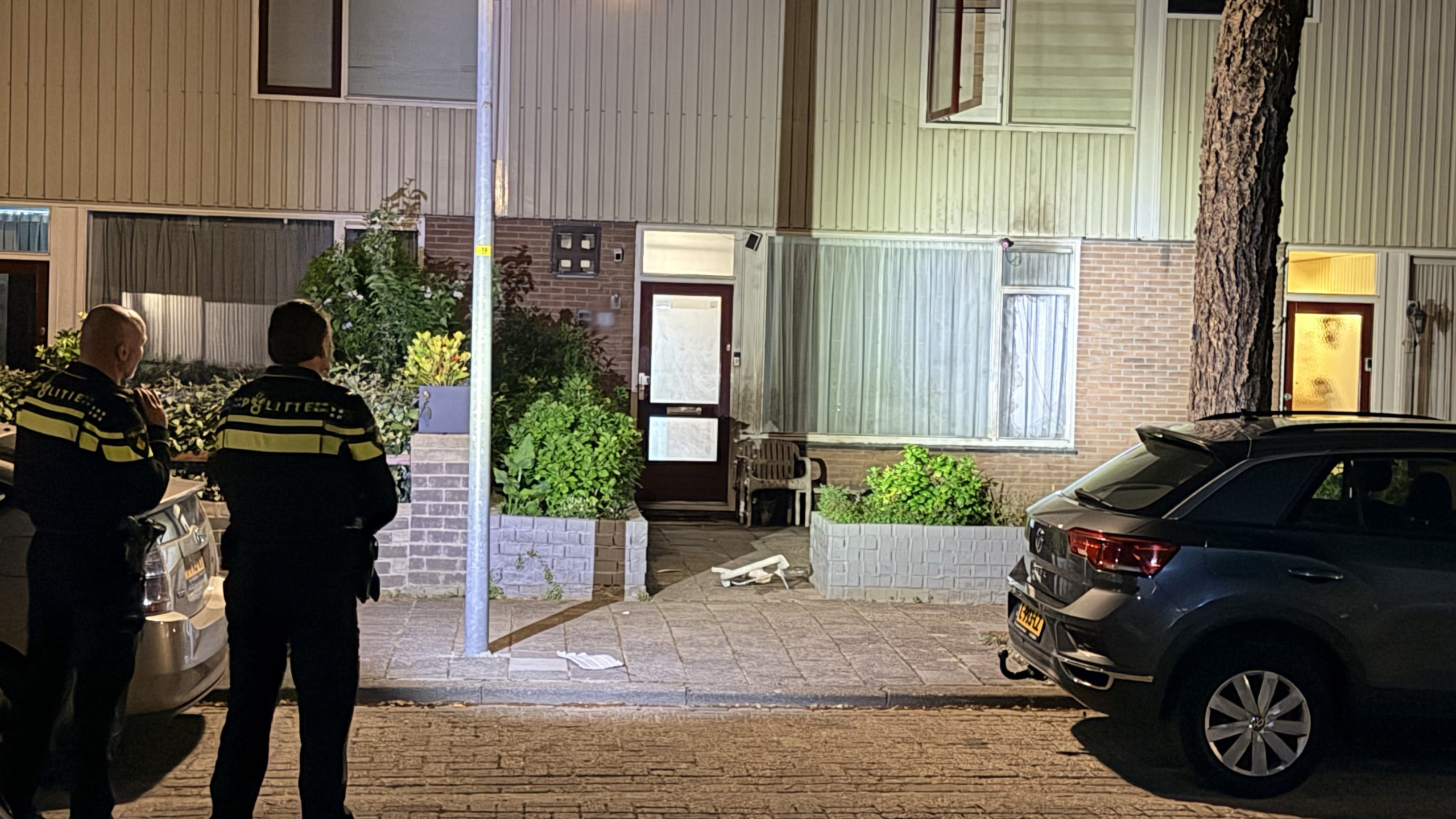 Twee politieagenten staan 's nachts voor een huis, kijkend naar de voordeur met een fiets op de grond.