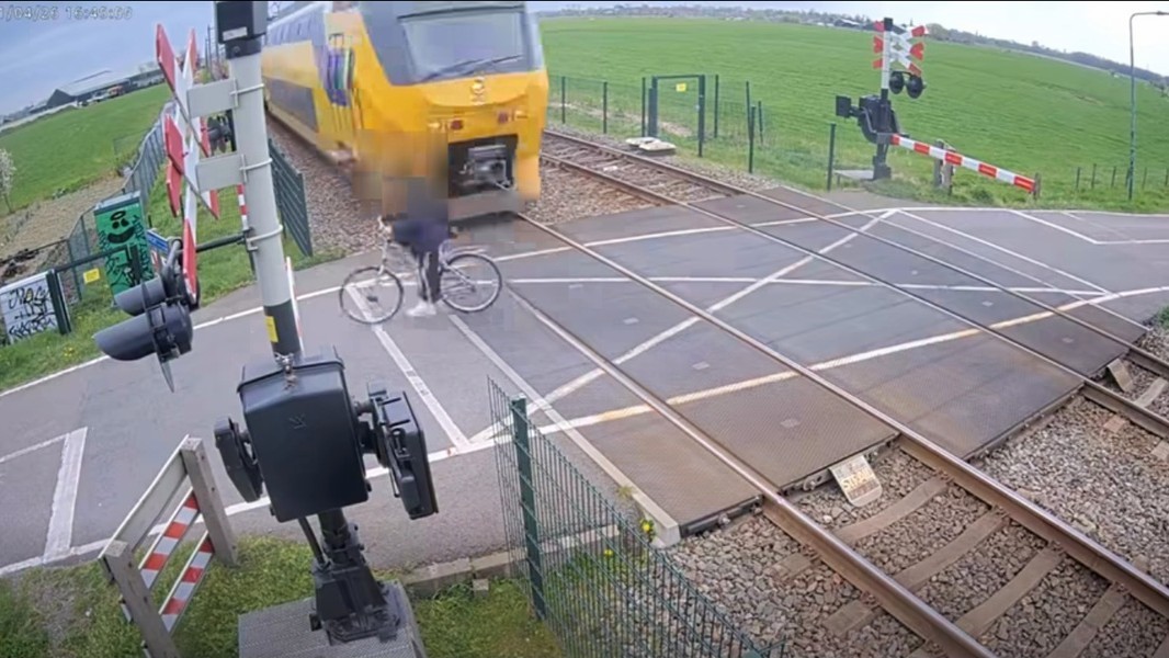 Een persoon steekt met een fiets een spoorwegovergang over terwijl een gele trein nadert.