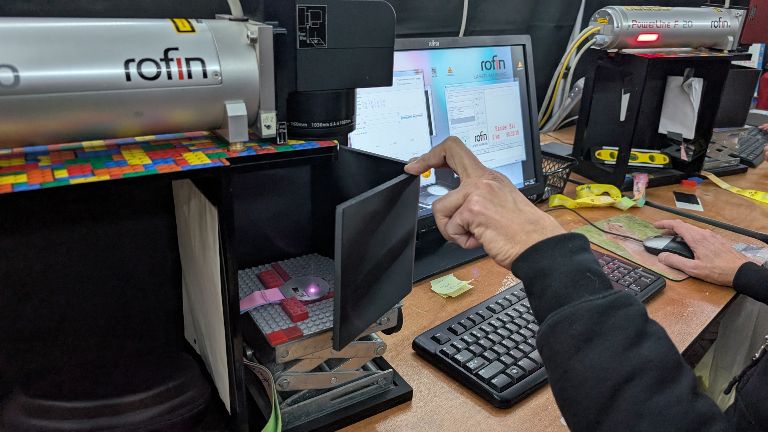 Persoon gebruikt een computer en lasergraveermachine met een monitor waarop "rofin LASER MARKING" te zien is.