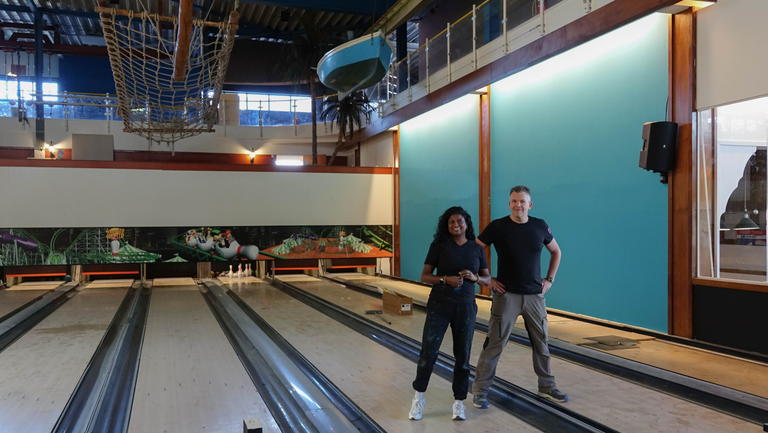 Twee mensen in een bowlingbaan, naast elkaar poserend tussen de lege banen.