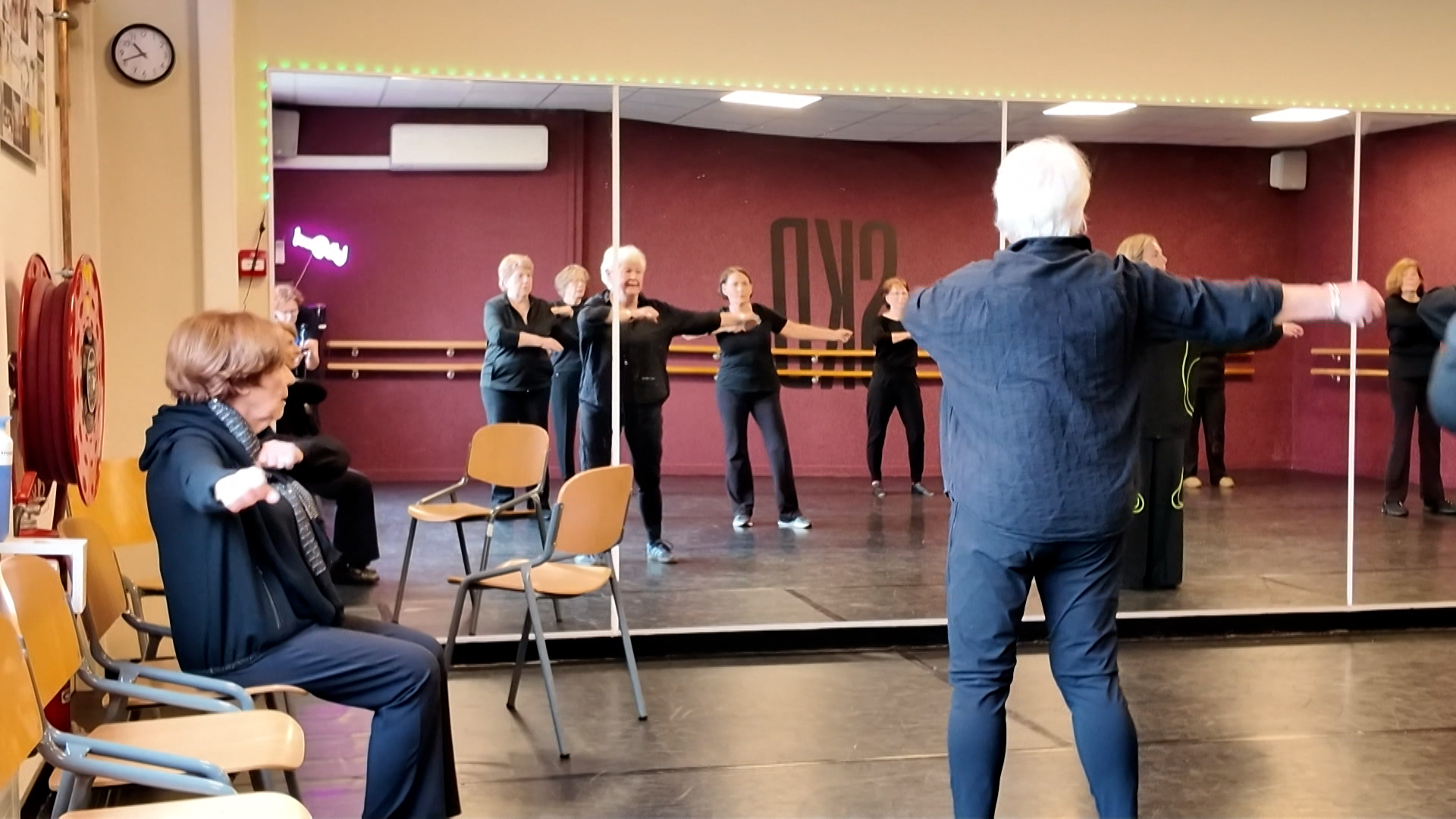 Een groep ouderen volgt een dansles in een spiegelzaal, geleid door een instructeur.