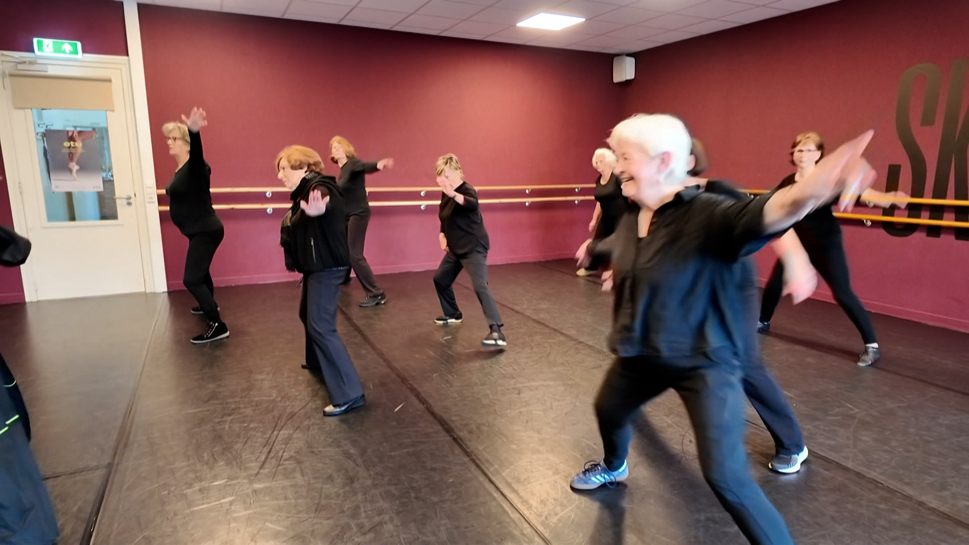 Groep oudere vrouwen doet een dansles in een studio met paarse muren.