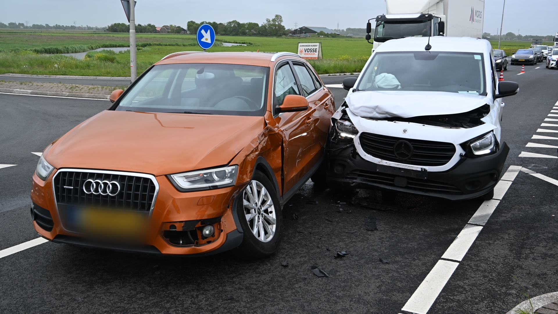 Een oranje Audi en een witte Mercedes bestelwagen zijn betrokken bij een aanrijding op een kruispunt.
