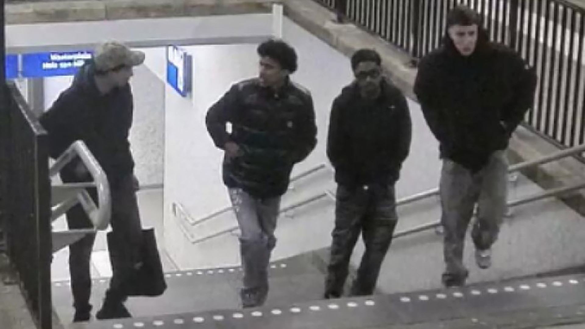 Vier personen lopen samen een trap op in een stationsomgeving.