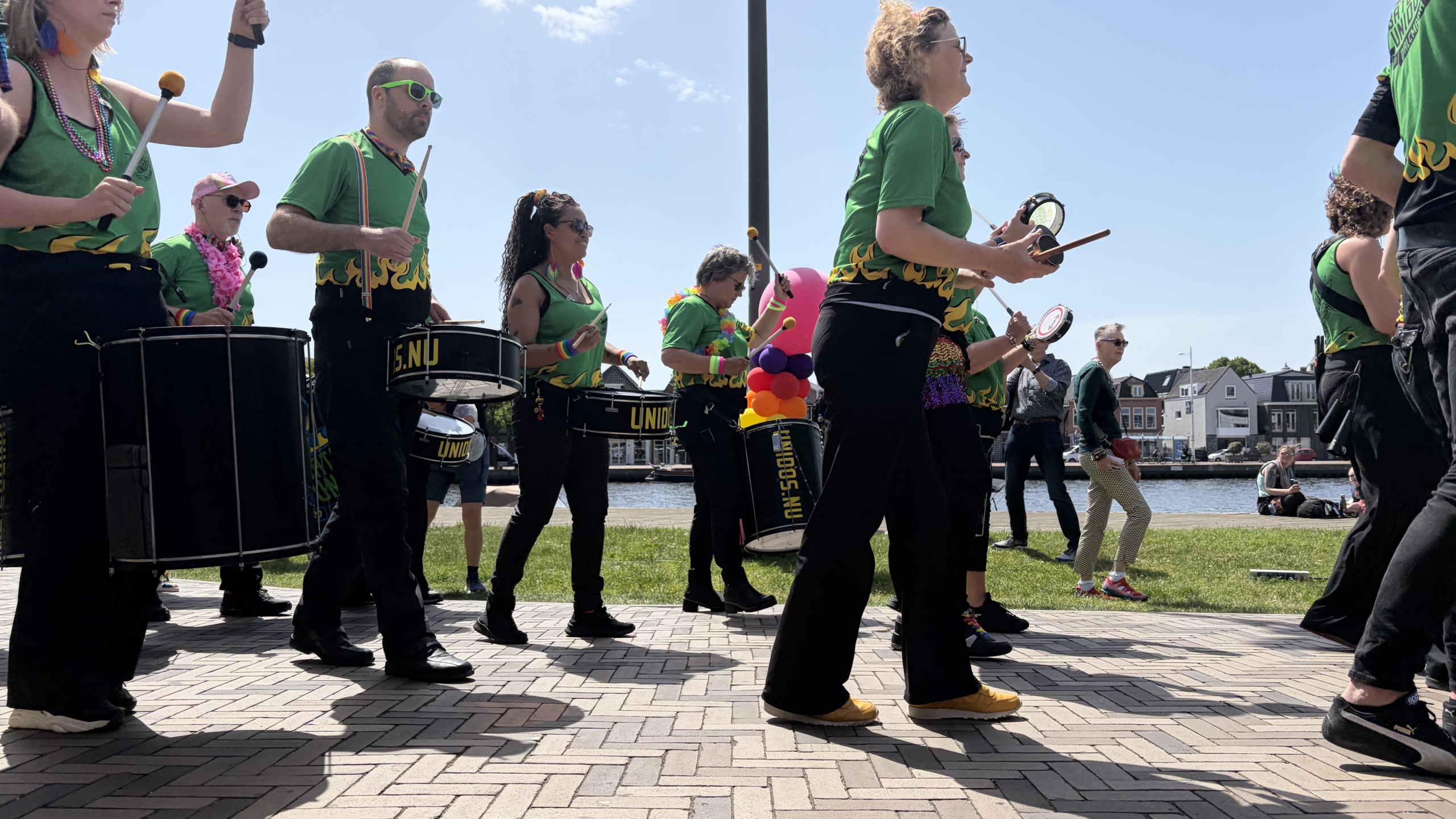 Een groep muzikanten in groene shirts speelt op trommels tijdens een evenement buiten bij zonnig weer.
