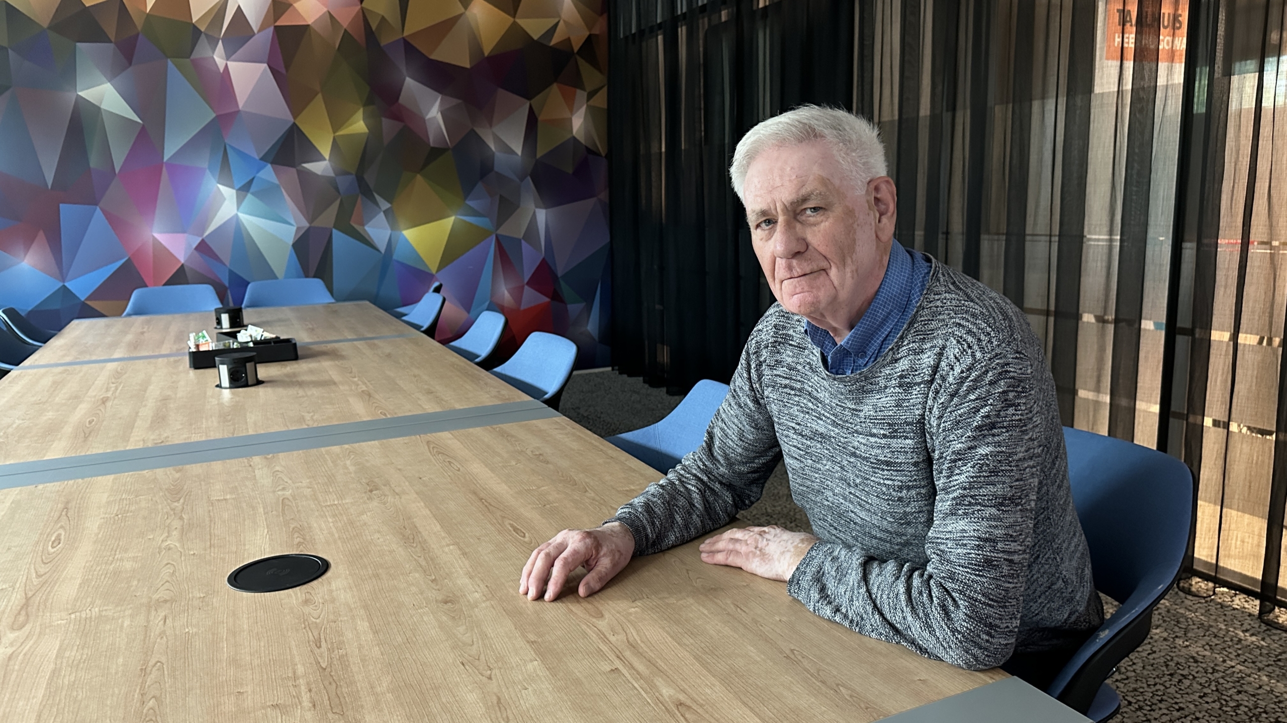Man zit aan een tafel in een vergaderzaal met kleurrijke geometrische muurdecoratie.