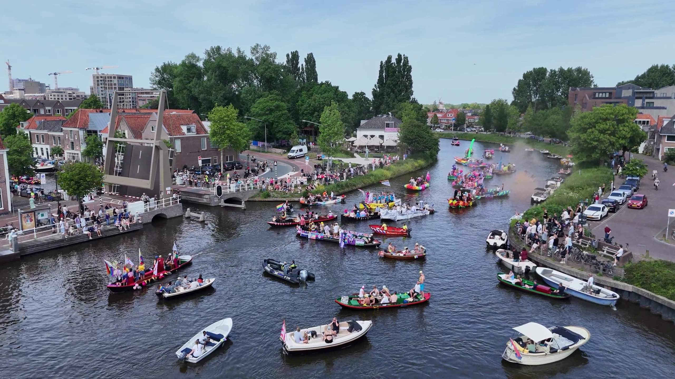 Een drukke waterparade met versierde boten en toeschouwers langs de oevers in een stadse omgeving.