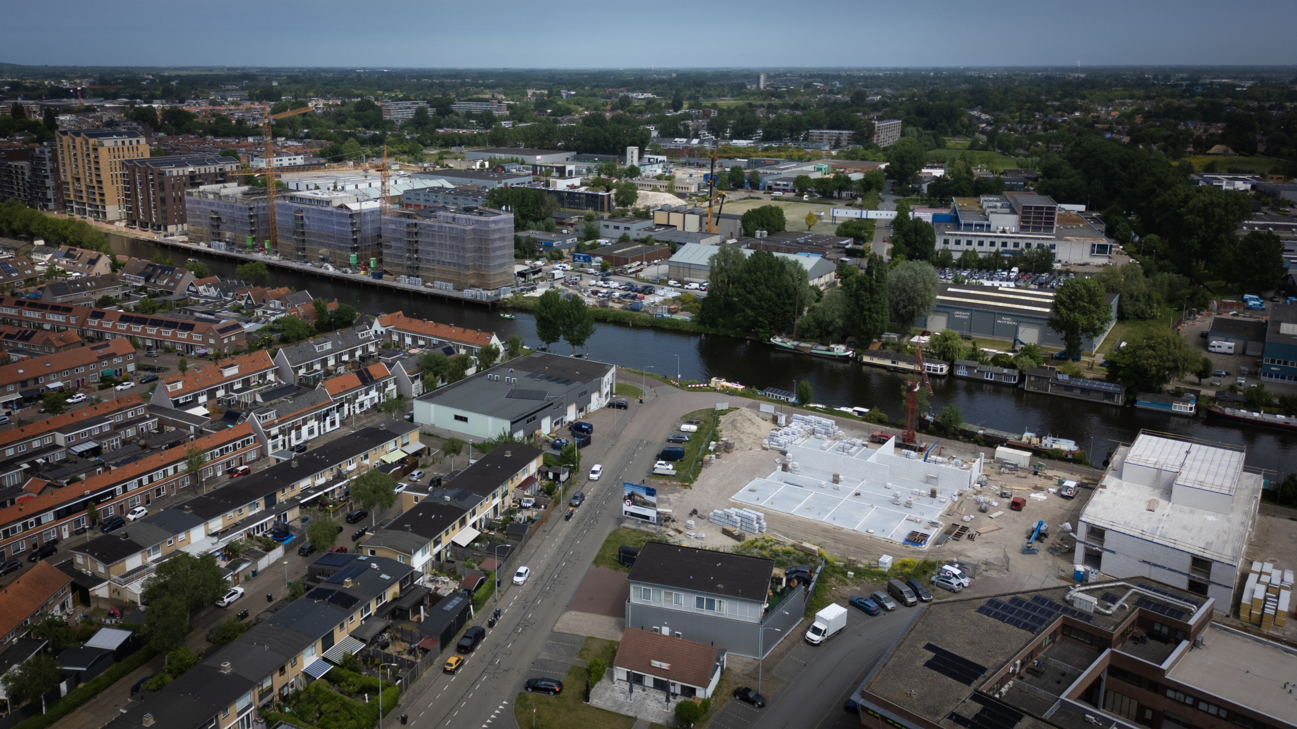 Luchtfoto van een stedelijk gebied met woningen, een bouwplaats en gebouwen langs een kanaal.