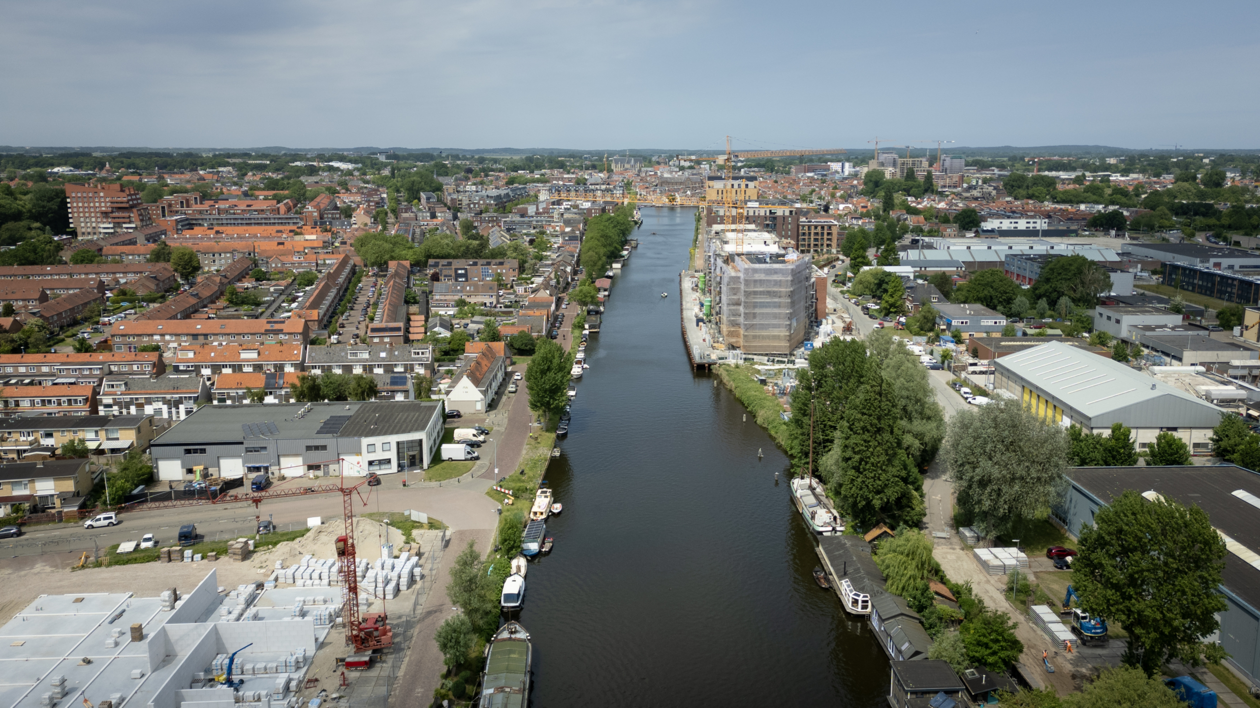 Luchtfoto van een stad met rode daken en een kanaal met boten, omgeven door woonblokken en industriële gebouwen.