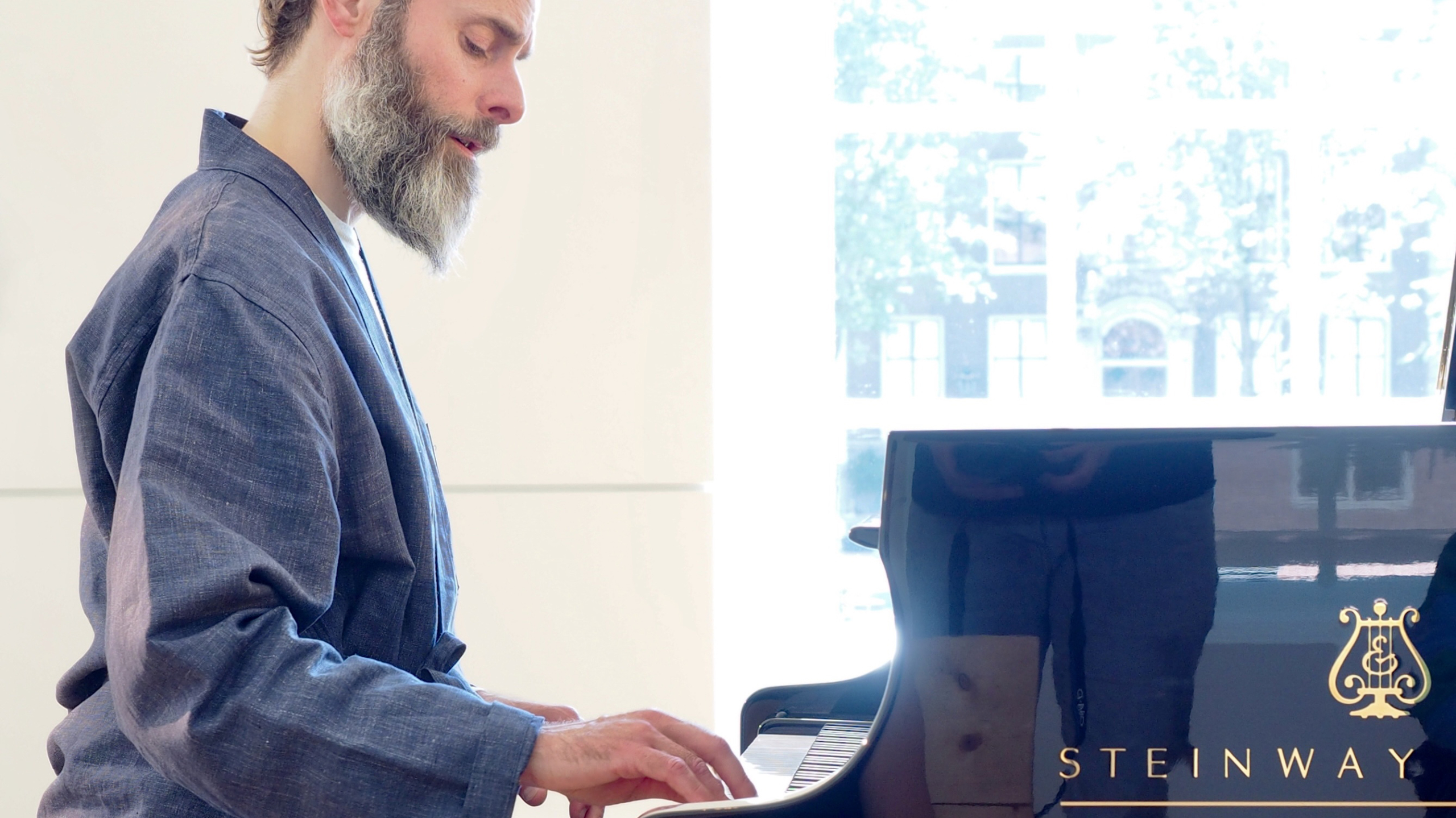 Man speelt piano in een lichte ruimte, met het merk Steinway zichtbaar op de piano.