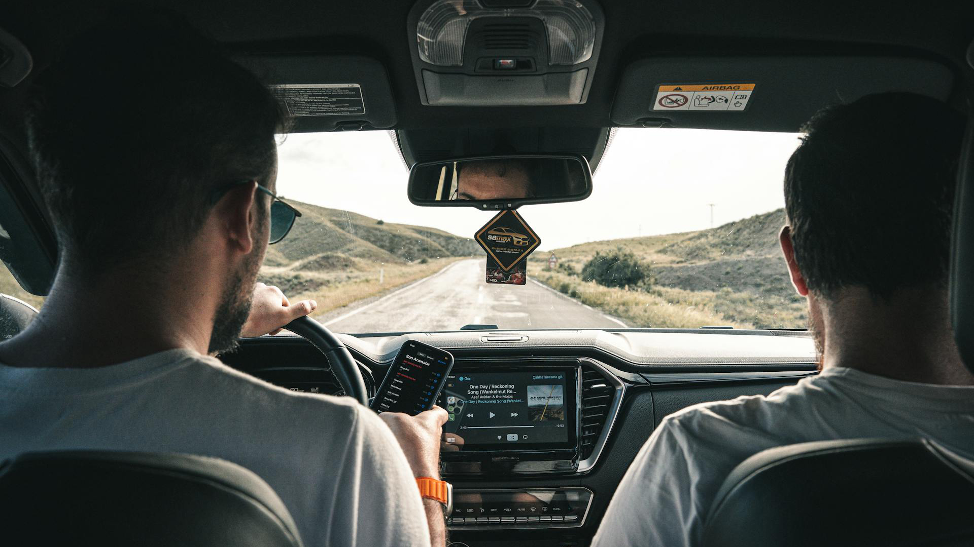 Twee personen zitten in een auto, een bestuurder kijkt naar de weg, terwijl de ander op een smartphone kijkt.