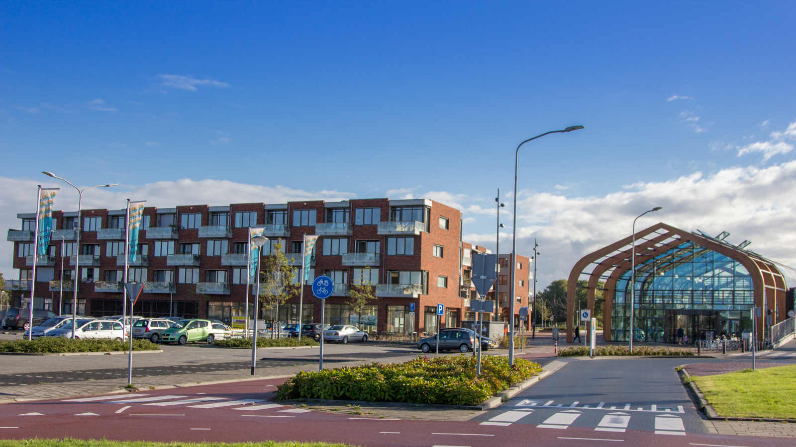 Modern gebouw met glazen entree naast een rood bakstenen appartementencomplex, met fietsenrekken op de voorgrond.