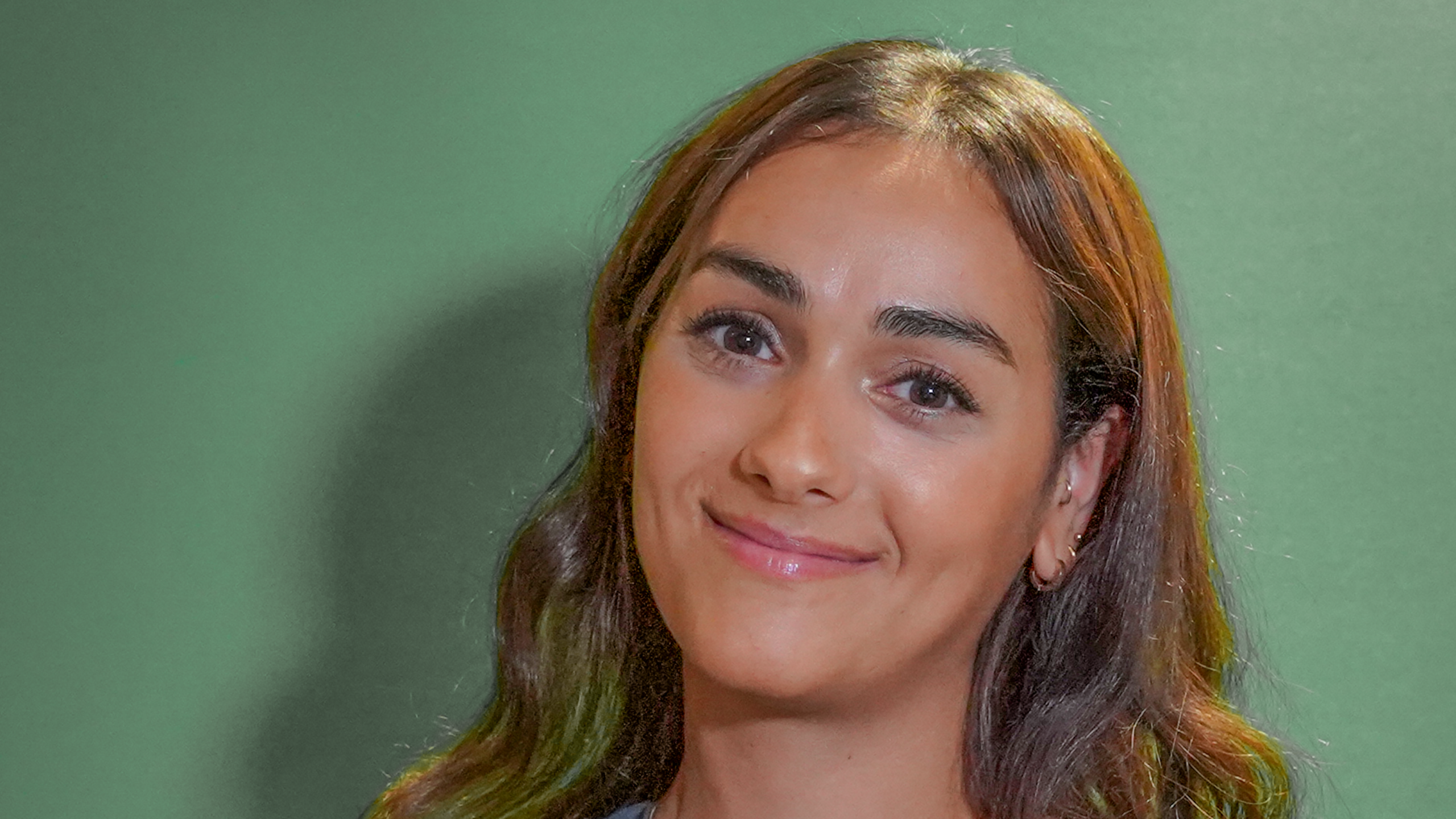 Een vrouw met lang donker haar en een vriendelijke glimlach tegen een groene achtergrond.