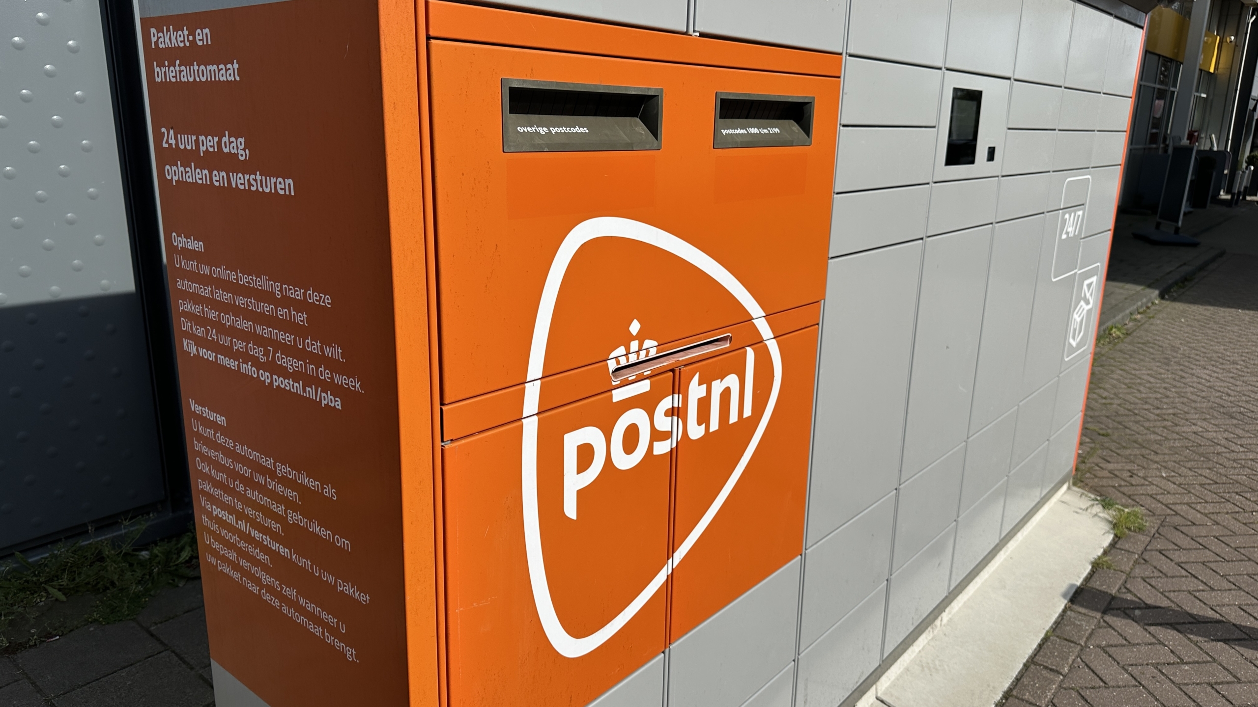 Oranje PostNL pakket- en brievenautomaat met opschriften voor ophalen en verzenden 24 uur per dag.