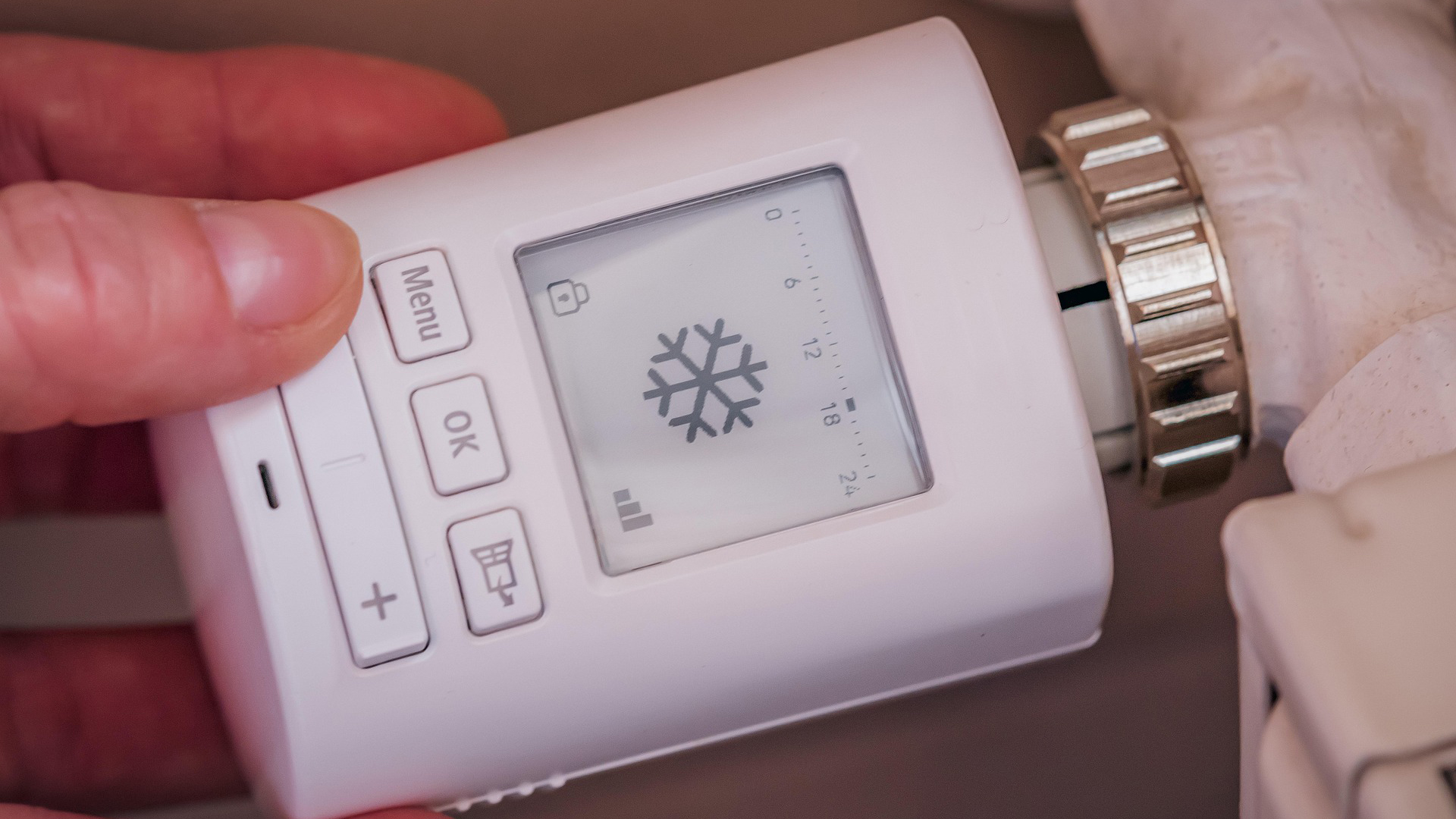 Een hand bedient een digitale thermostaatknop met een sneeuwvlokpictogram op het scherm.