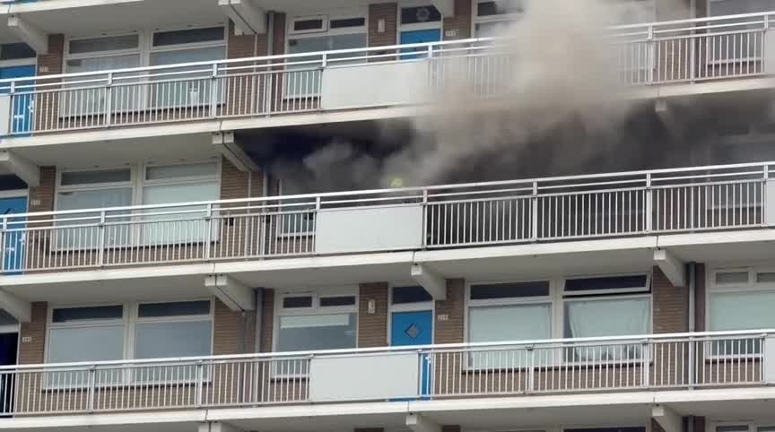 Rook stroomt uit een raam op de bovenste verdieping van een flatgebouw.