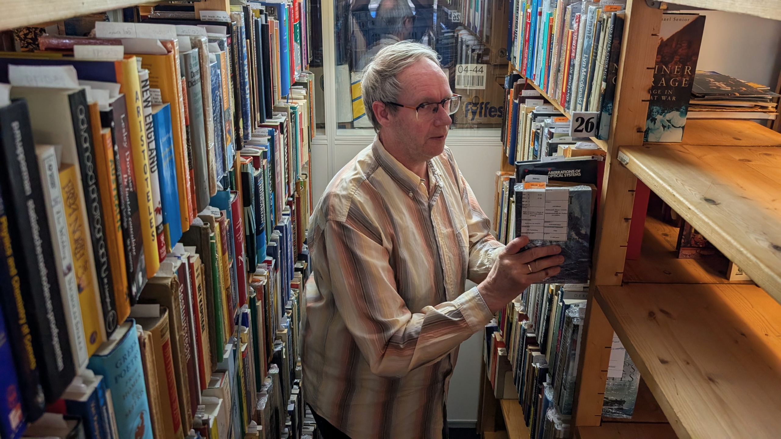 Man zoekt boek in een smalle gang van een bibliotheek, omringd door volle boekenplanken.