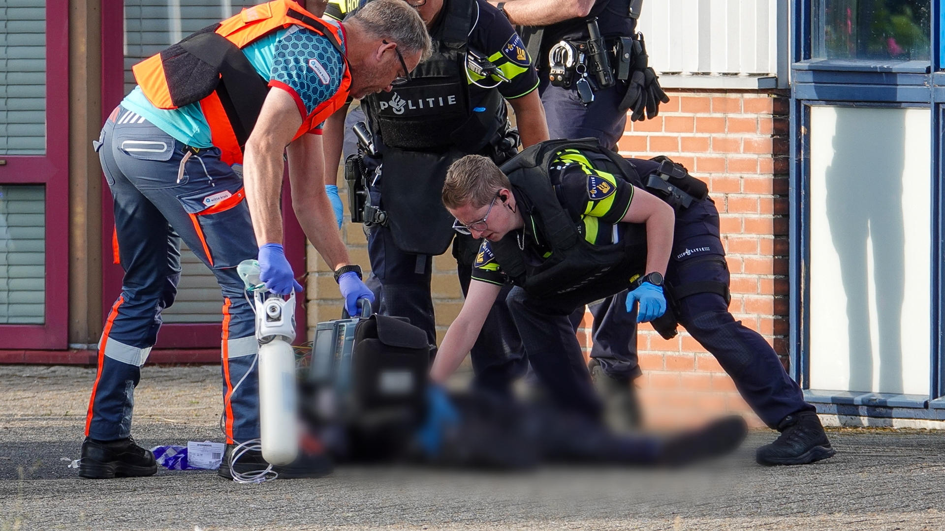 Politieagenten en een hulpverlener verzorgen een persoon op de grond met medische apparatuur.