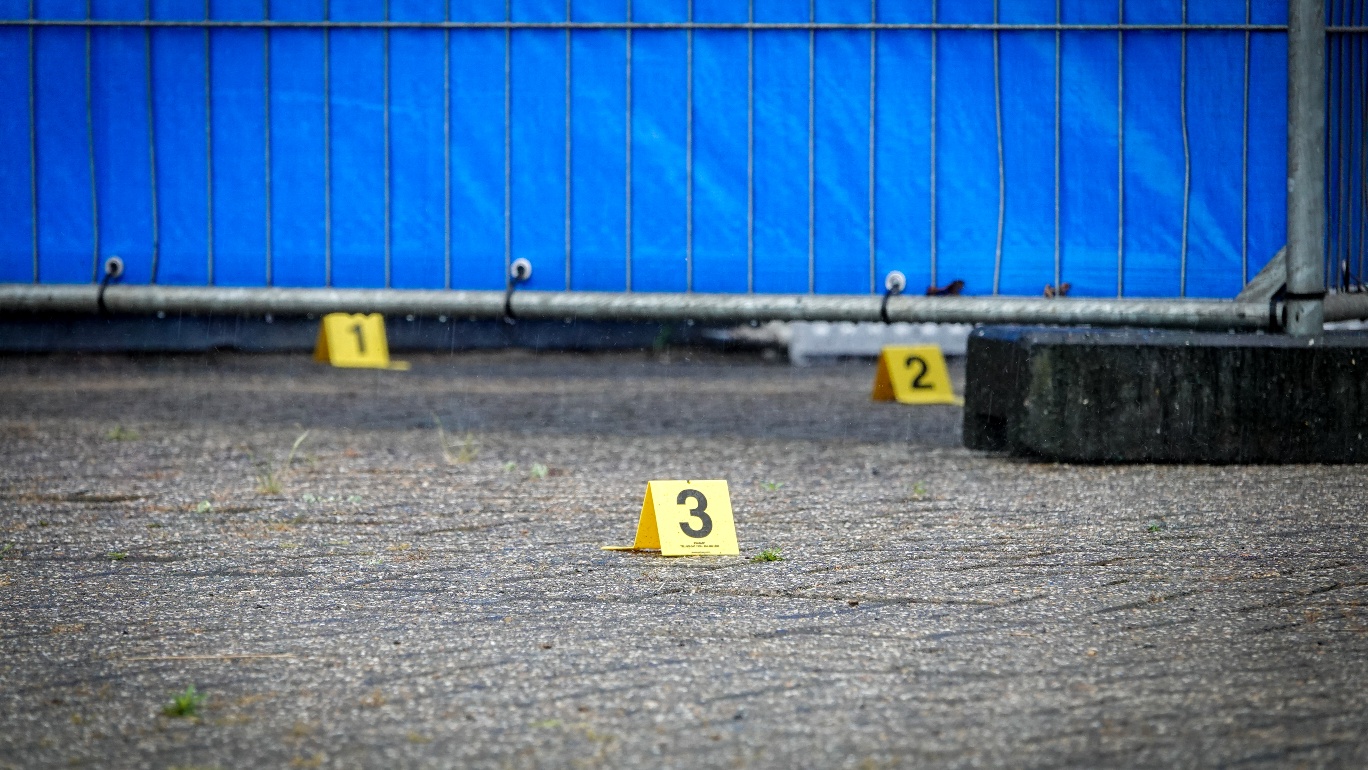 Drie gele nummermarkeringen op de grond voor een blauw bouwhek.