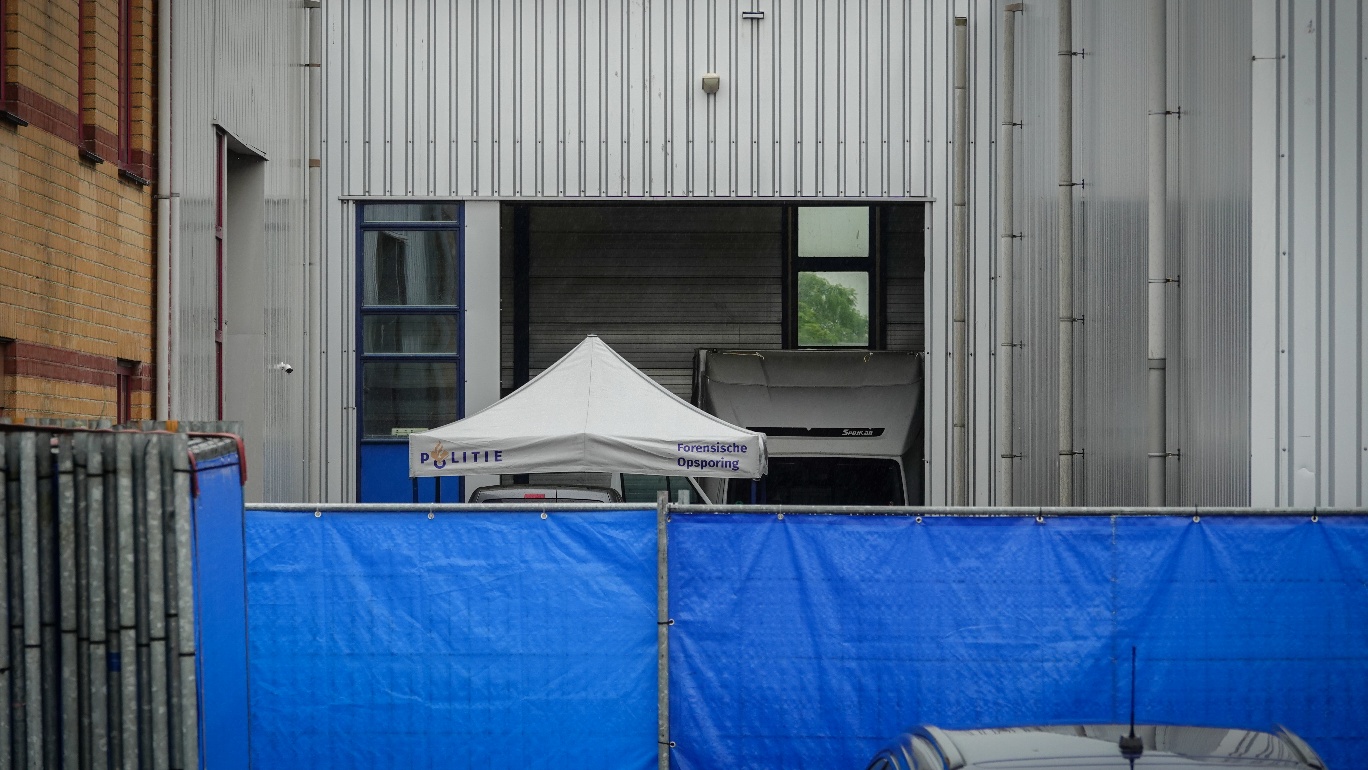 Een politie tent voor forensisch onderzoek staat opgesteld naast een gebouw met een blauwe afscherming ervoor.
