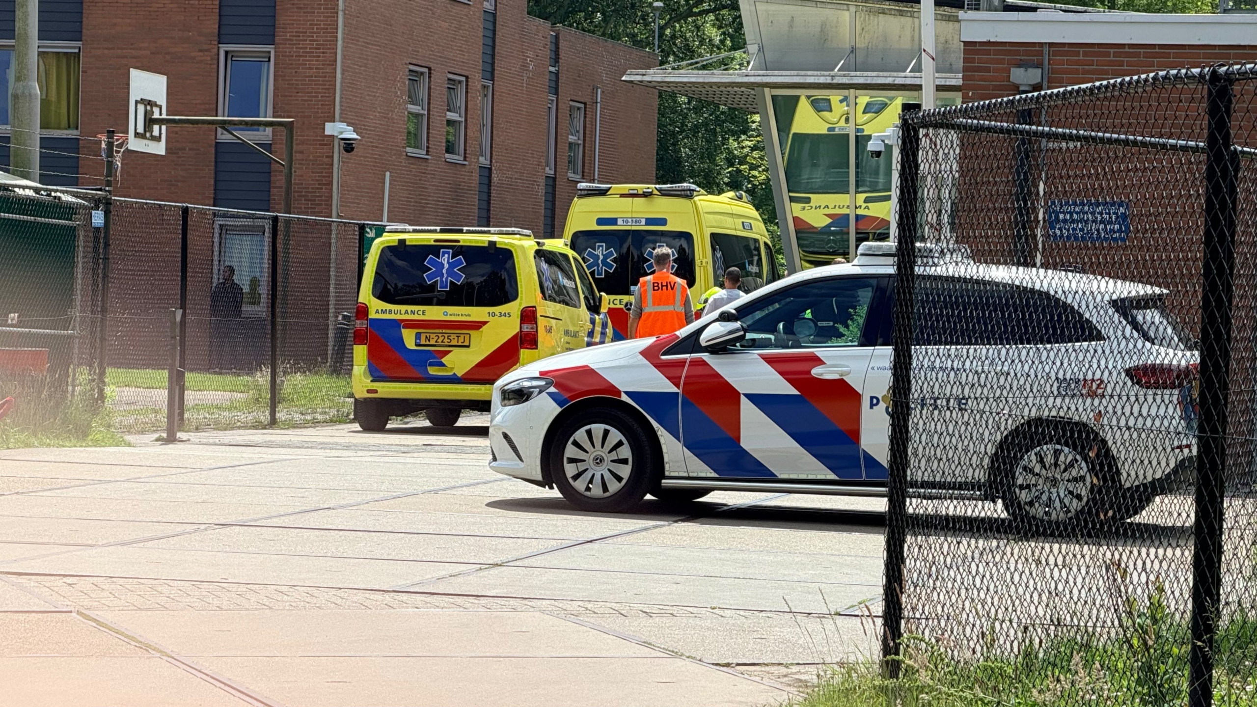 Politie- en ambulances staan geparkeerd bij een gebouw, met een persoon in een BHV-vest op de voorgrond.