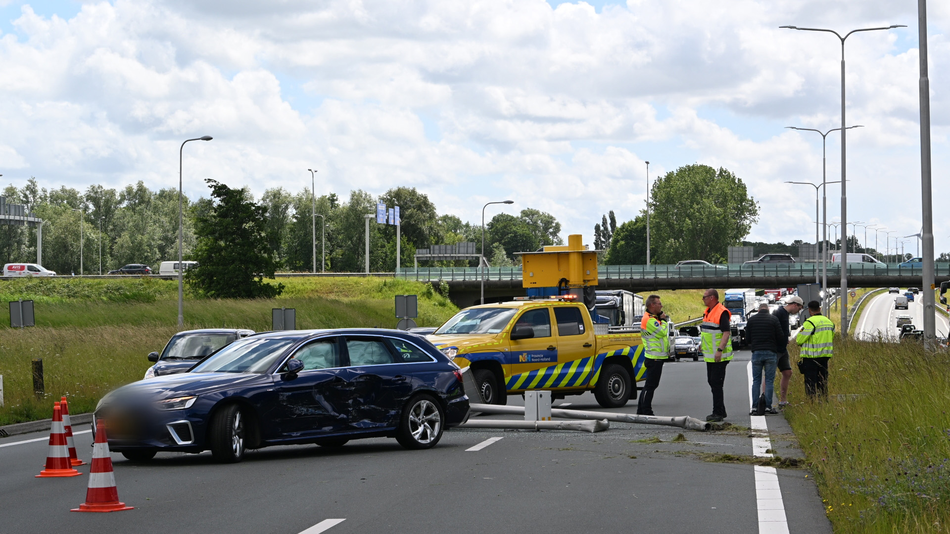 Twee beschadigde auto's en een omgevallen verkeerspaal op de weg, omgeven door mannen in fluorescerende kleding.