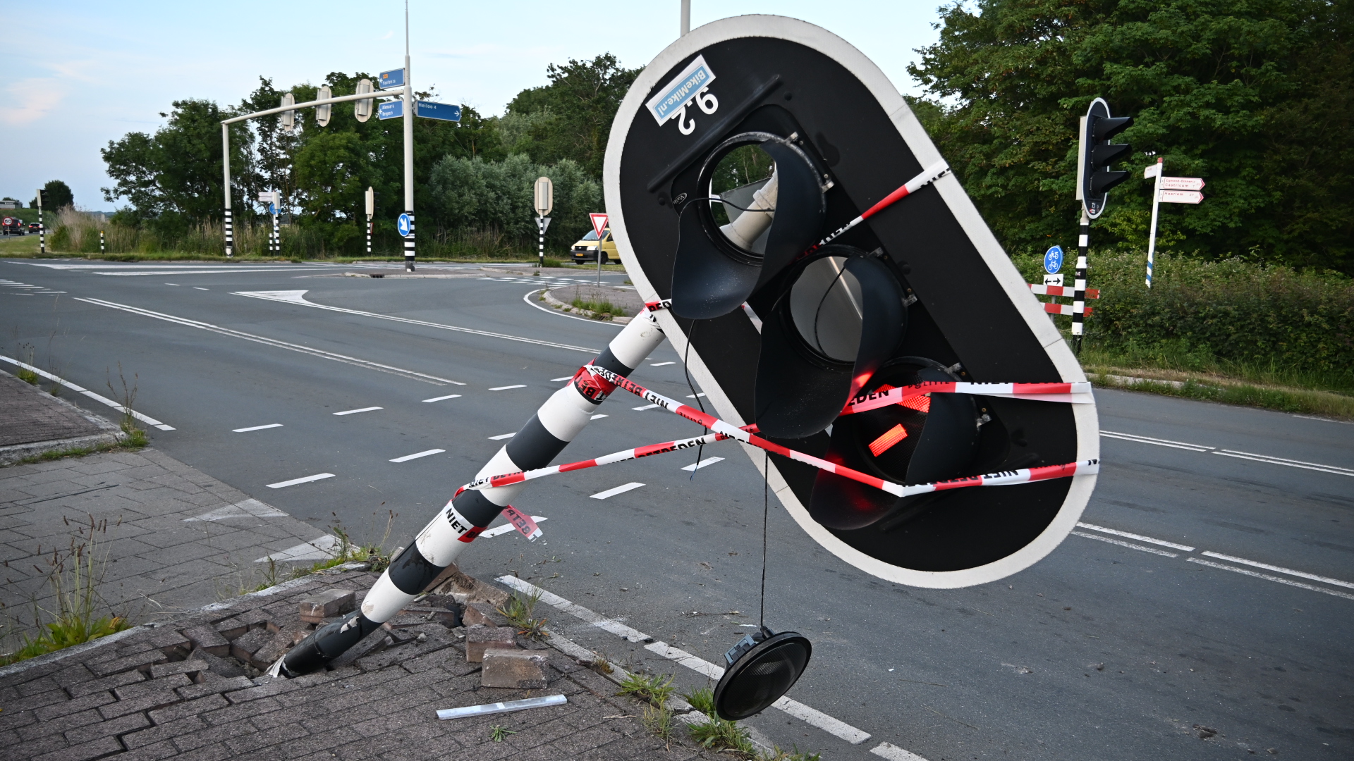 Een omgewaaide verkeerslichtenpaal ligt over een stoep, omringd door rood-wit waarschuwingslint.