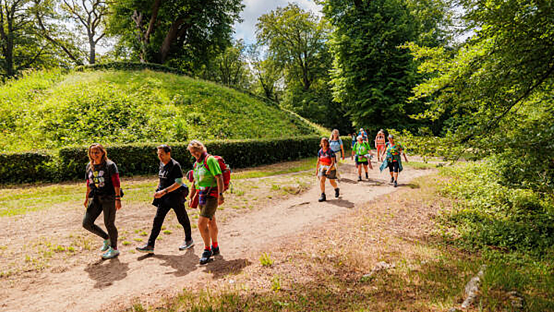 Groep mensen wandelt over een bospad, omgeven door groene bomen en struiken.