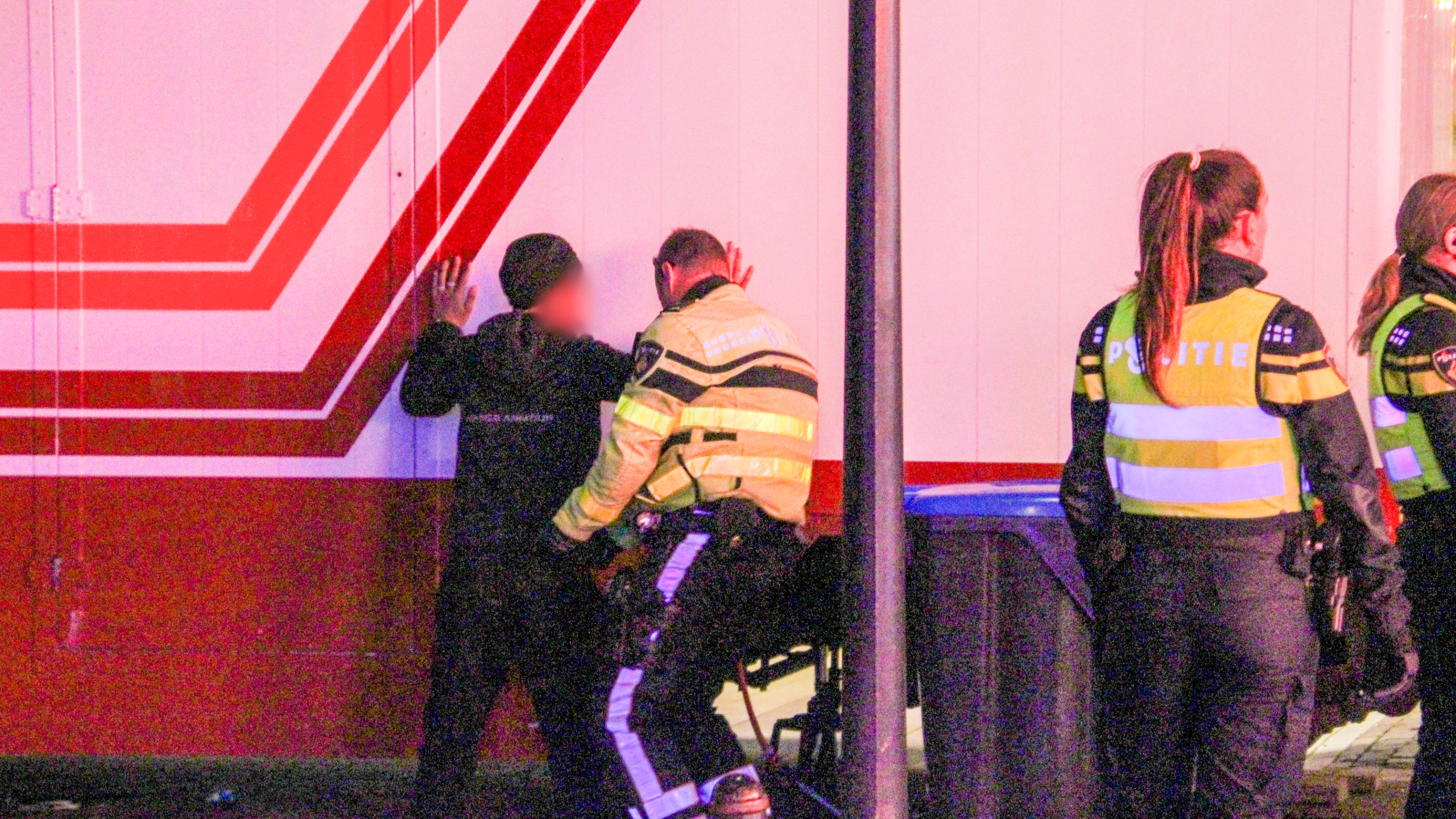 Politieagenten controleren een persoon tegen een muur met rode strepen.