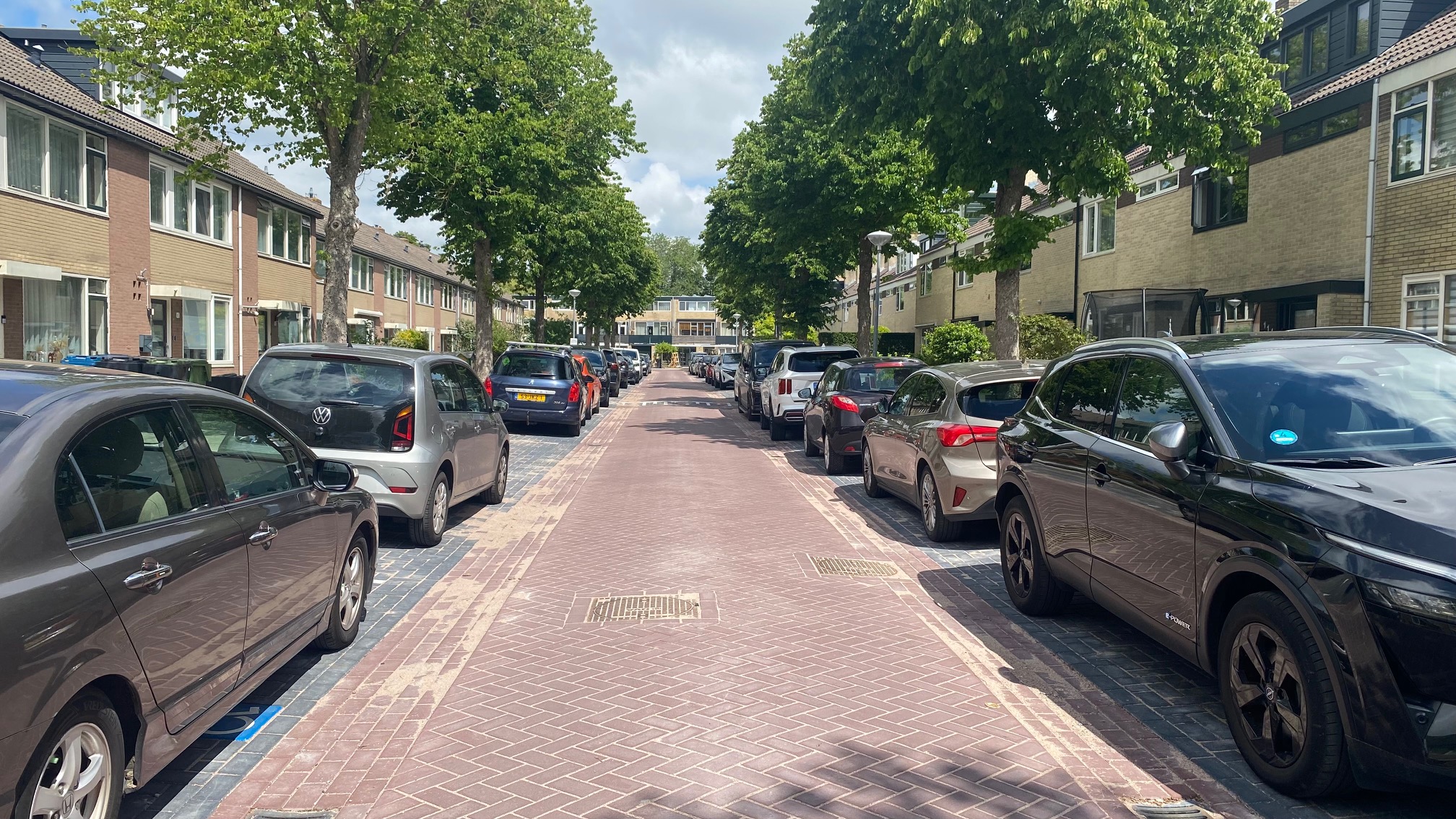 Een rustige woonstraat met bomen langs de zijkanten en auto's geparkeerd aan beide kanten van de weg.