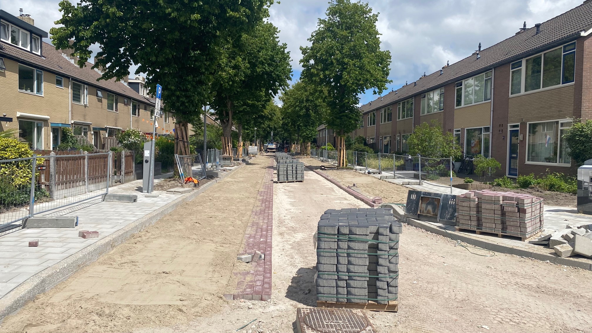 Wegwerkzaamheden in een woonwijk, met gestapelde stoeptegels en bomen langs de weg.