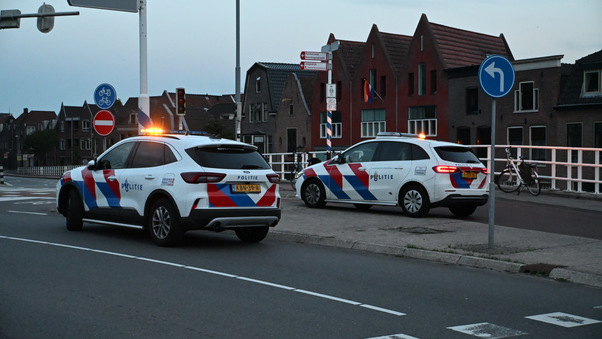 Twee politieauto's staan geparkeerd op een weg bij een kruispunt in een woonwijk.