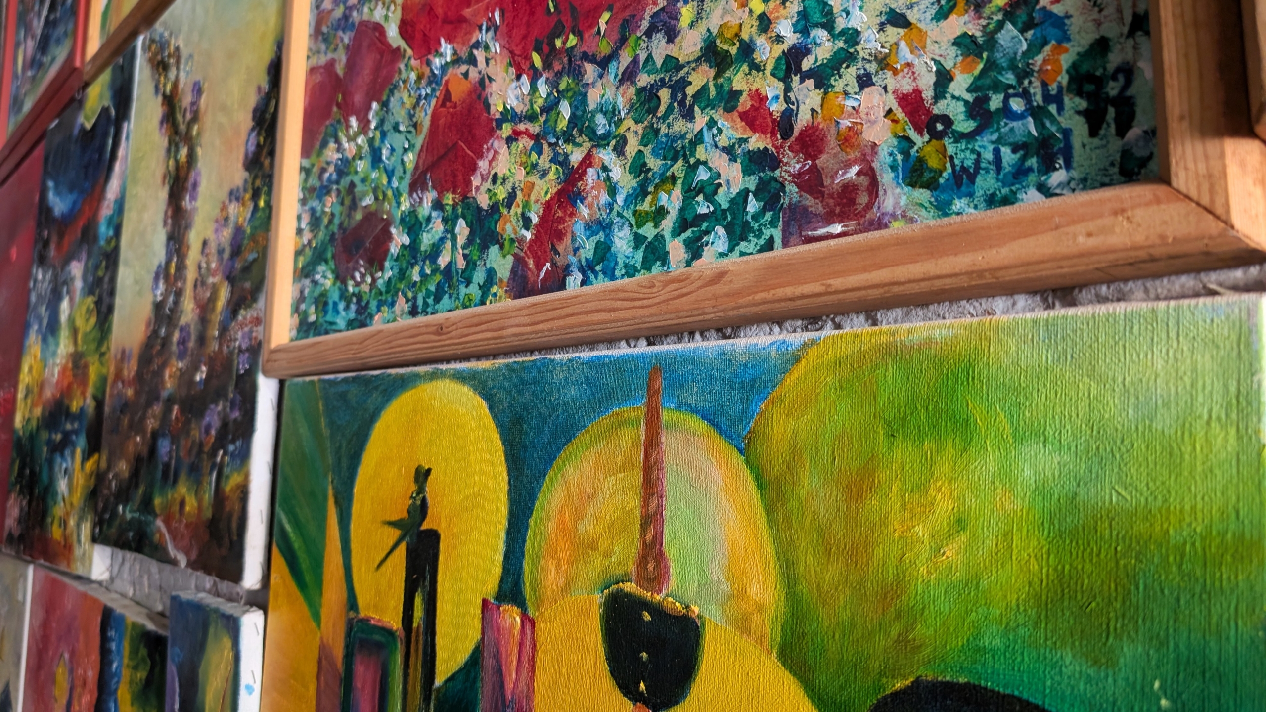 Een close-up van kleurrijke expressionistische schilderijen met abstracte vormen en felle tinten, hangend aan een muur.