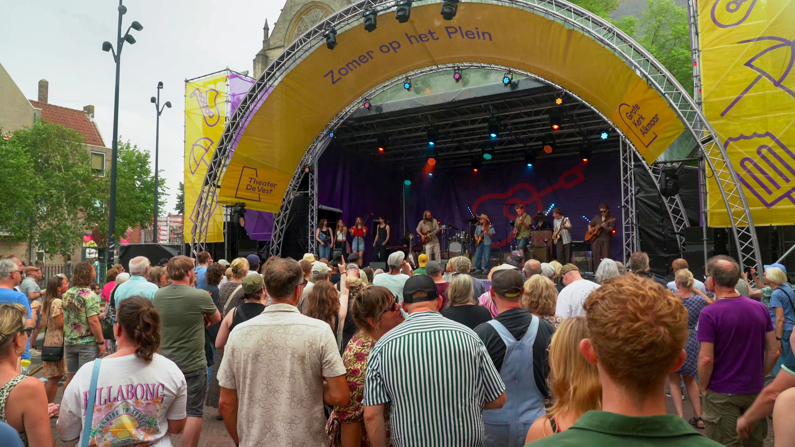 Openluchtconcert tijdens "Zomer op het Plein" met een groot publiek en een band die op het podium speelt.