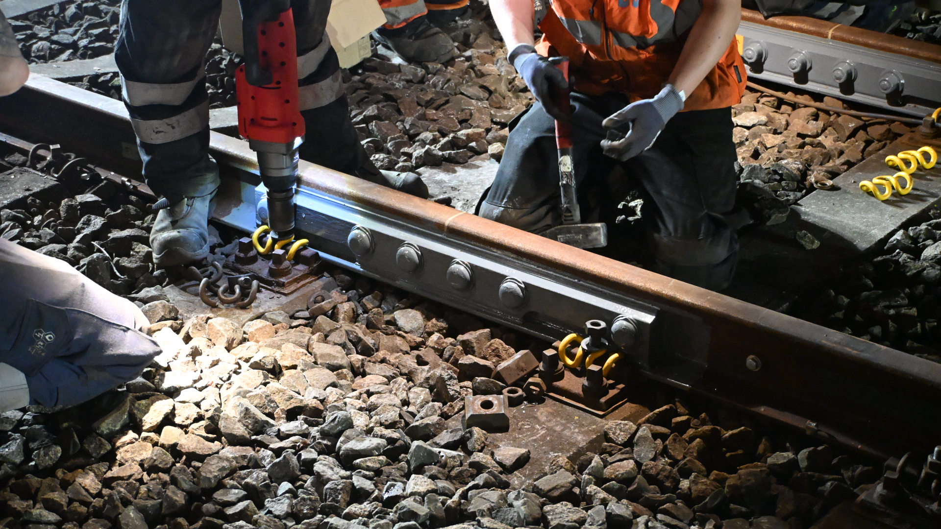 Werkers repareren een treinspoor met gereedschap, omringd door grind.