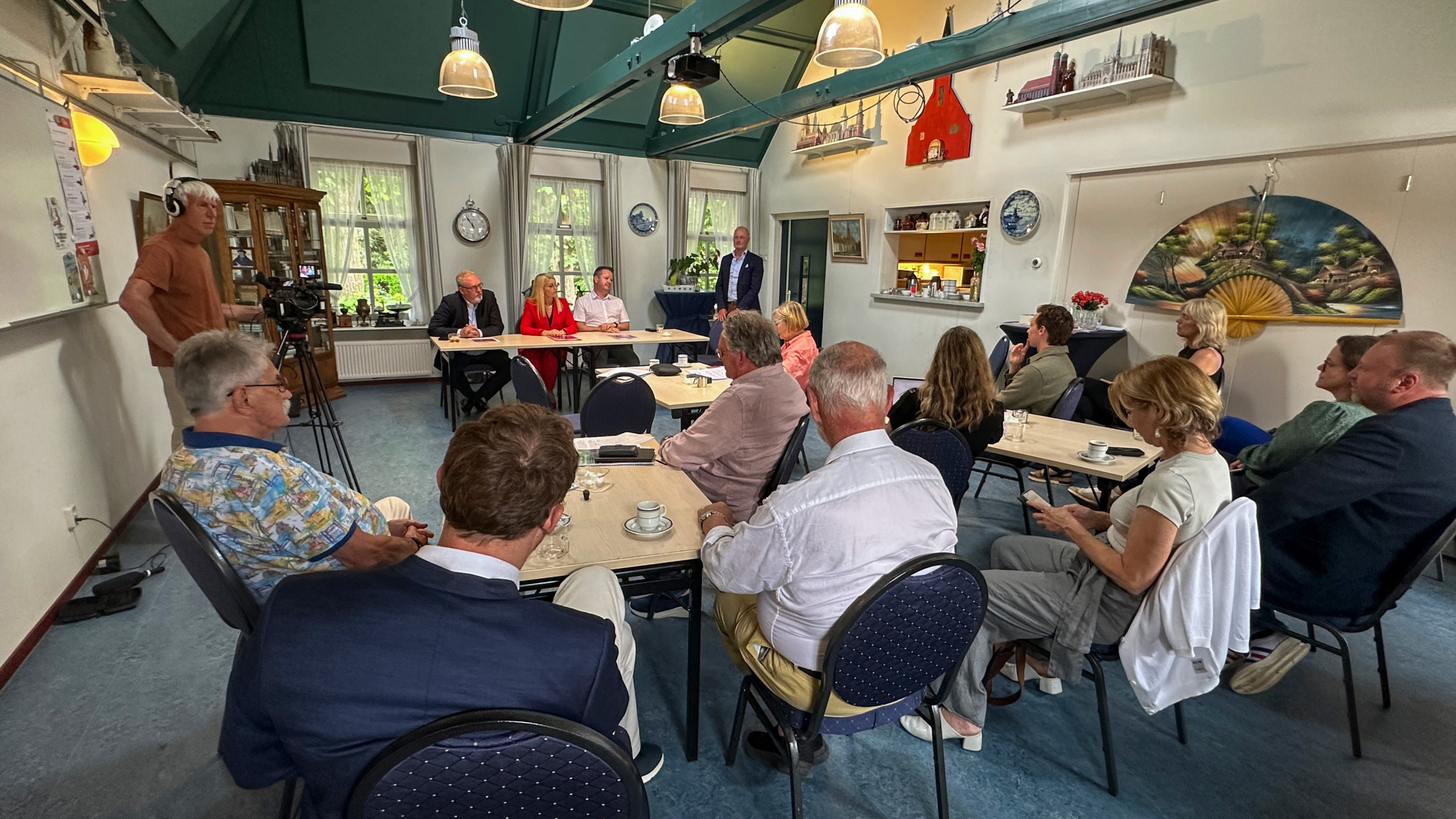 Een groep mensen zit aan tafels in een vergaderruimte, terwijl iemand een presentatie geeft.