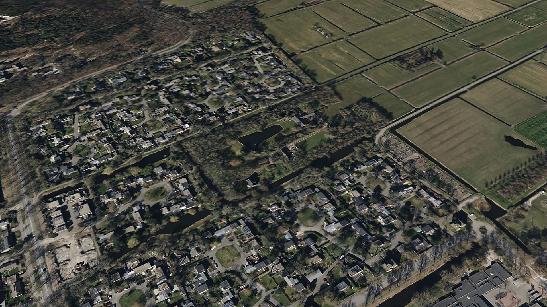 Luchtfoto van een woonwijk, omgeven door groene landbouwvelden en bossen.