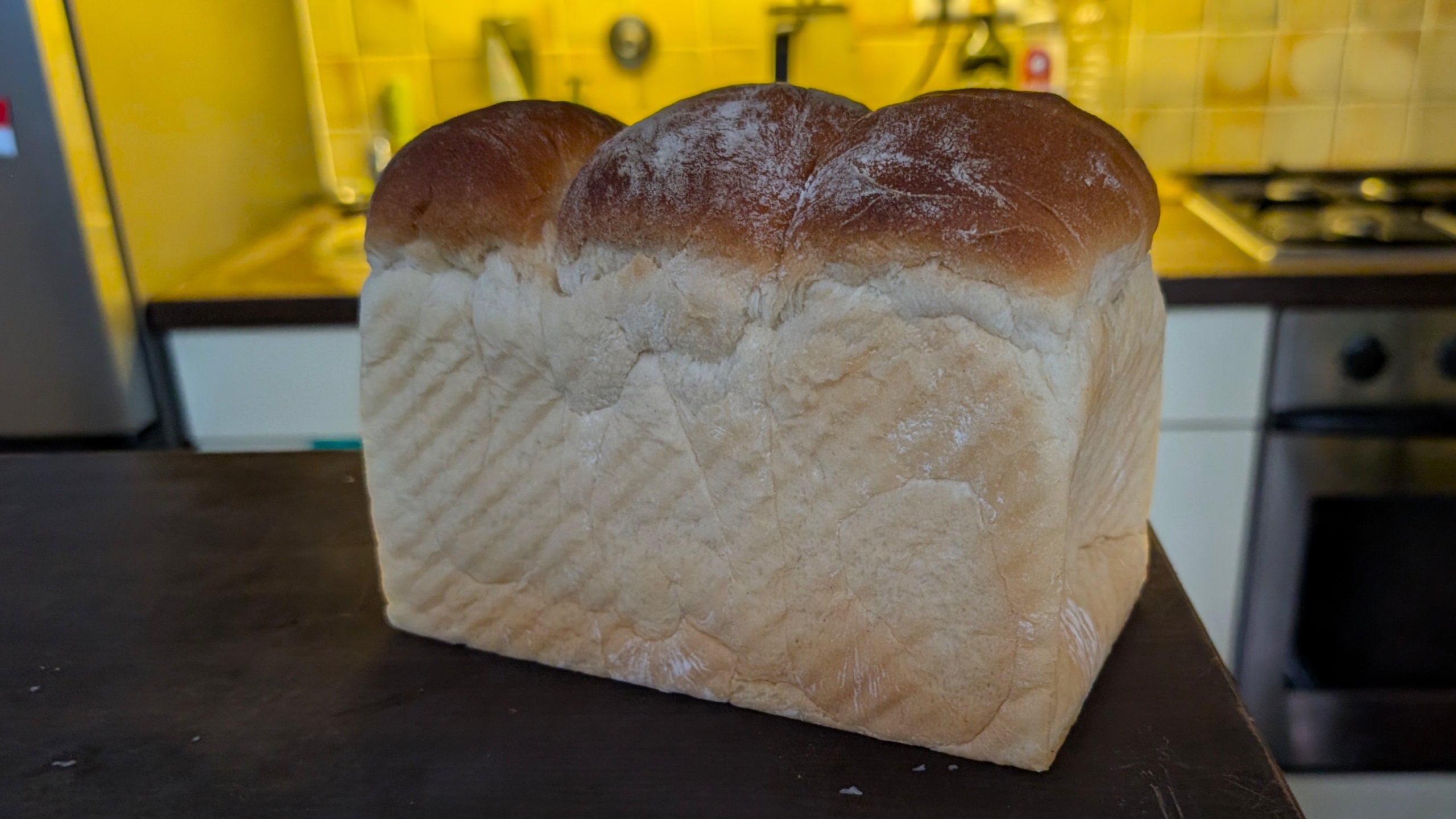 Een versgebakken brood met een gebruinde korst op een keukenblad in een gele keukenomgeving.
