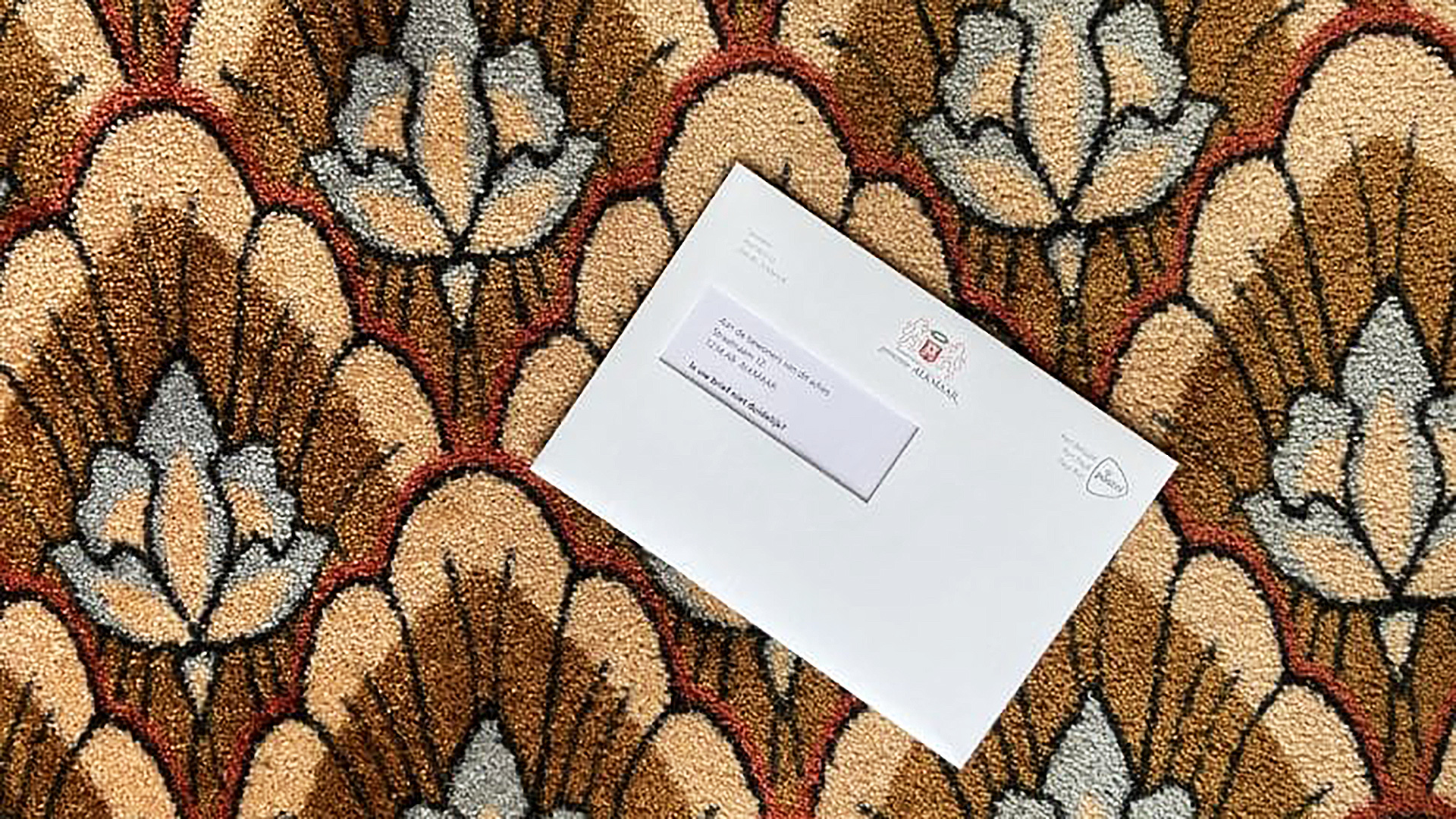 Een witte envelop met een adressticker ligt op een kleurrijk, bloemvormig tapijt.