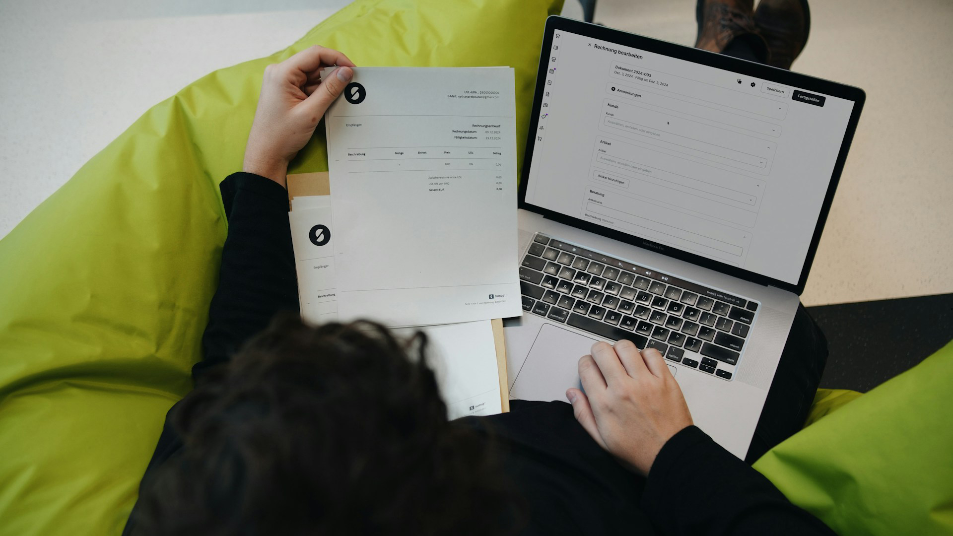 Persoon werkt op een laptop terwijl hij een document bekijkt, zittend op een groene zitzak.