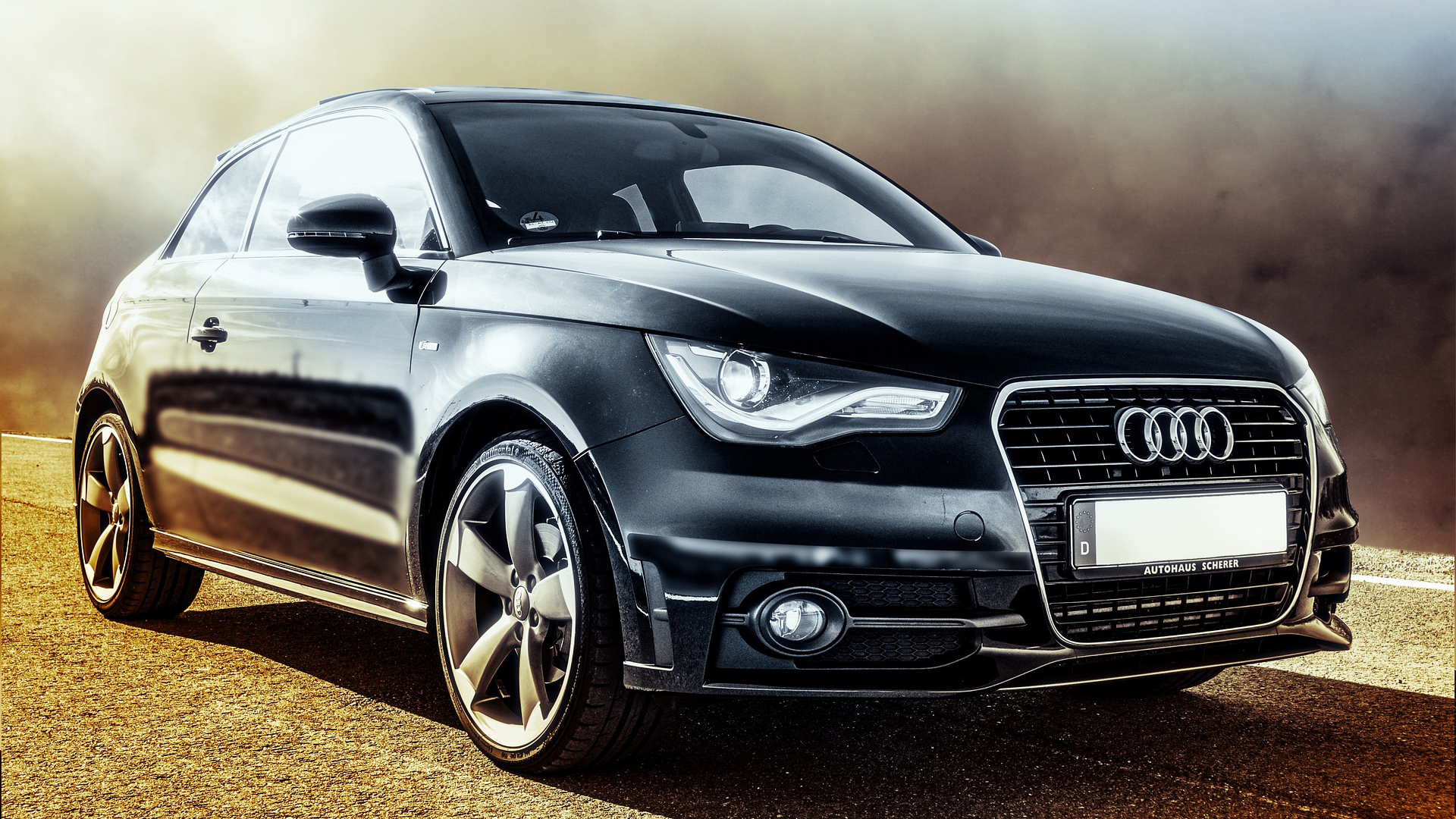Zwarte Audi auto op een weg in de zon, met kenmerkende grille en lichtmetalen velgen.