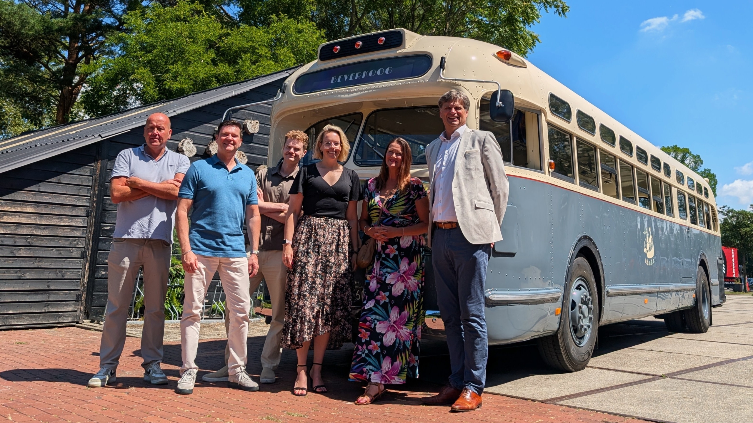 Een groep van zes mensen poseert voor een vintage bus met het woord "Beverkoog" op de bestemming.