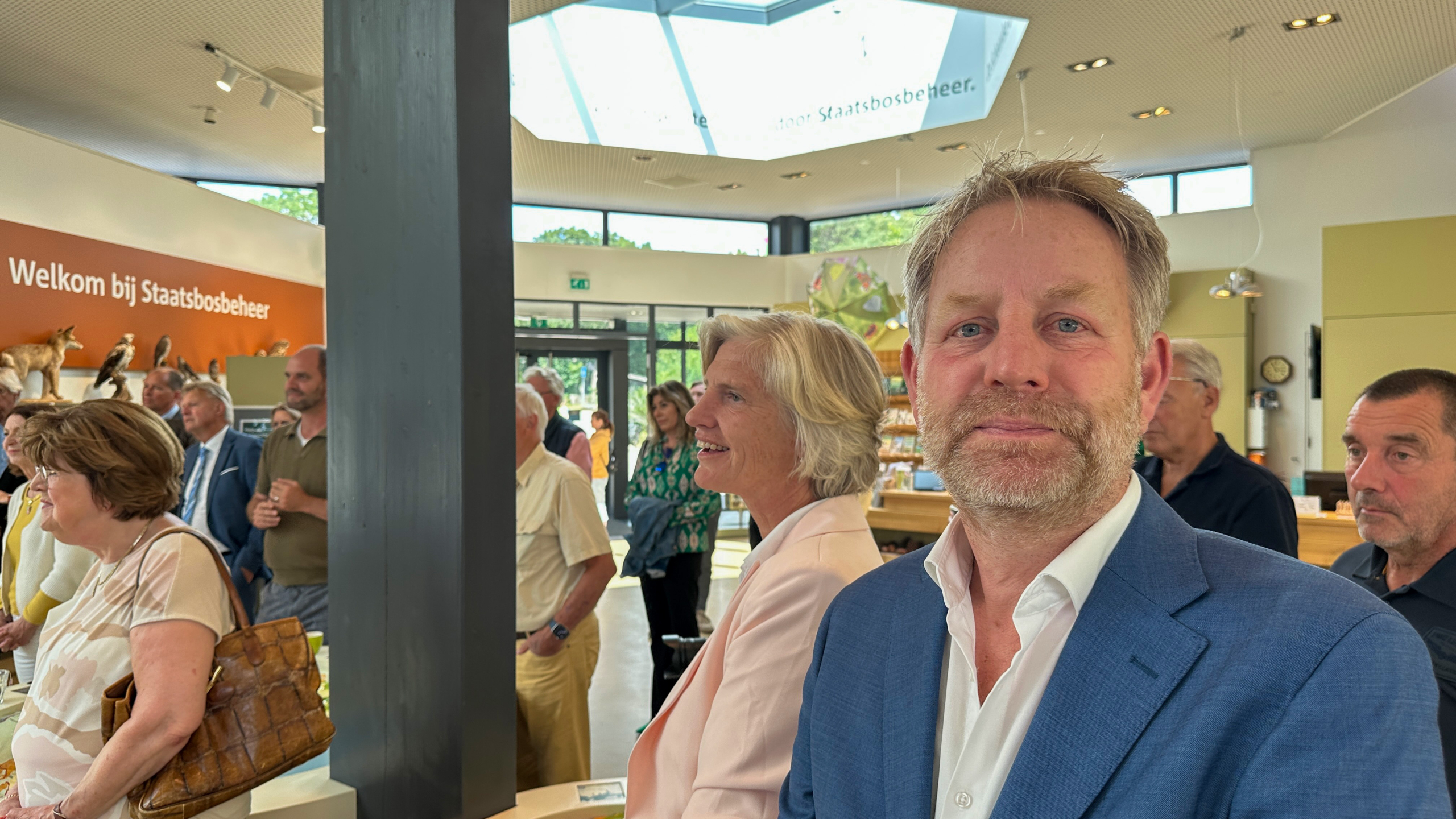 Mensen in een ontvangsthal met op de achtergrond de tekst "Welkom bij Staatsbosbeheer" en opgezette dieren.
