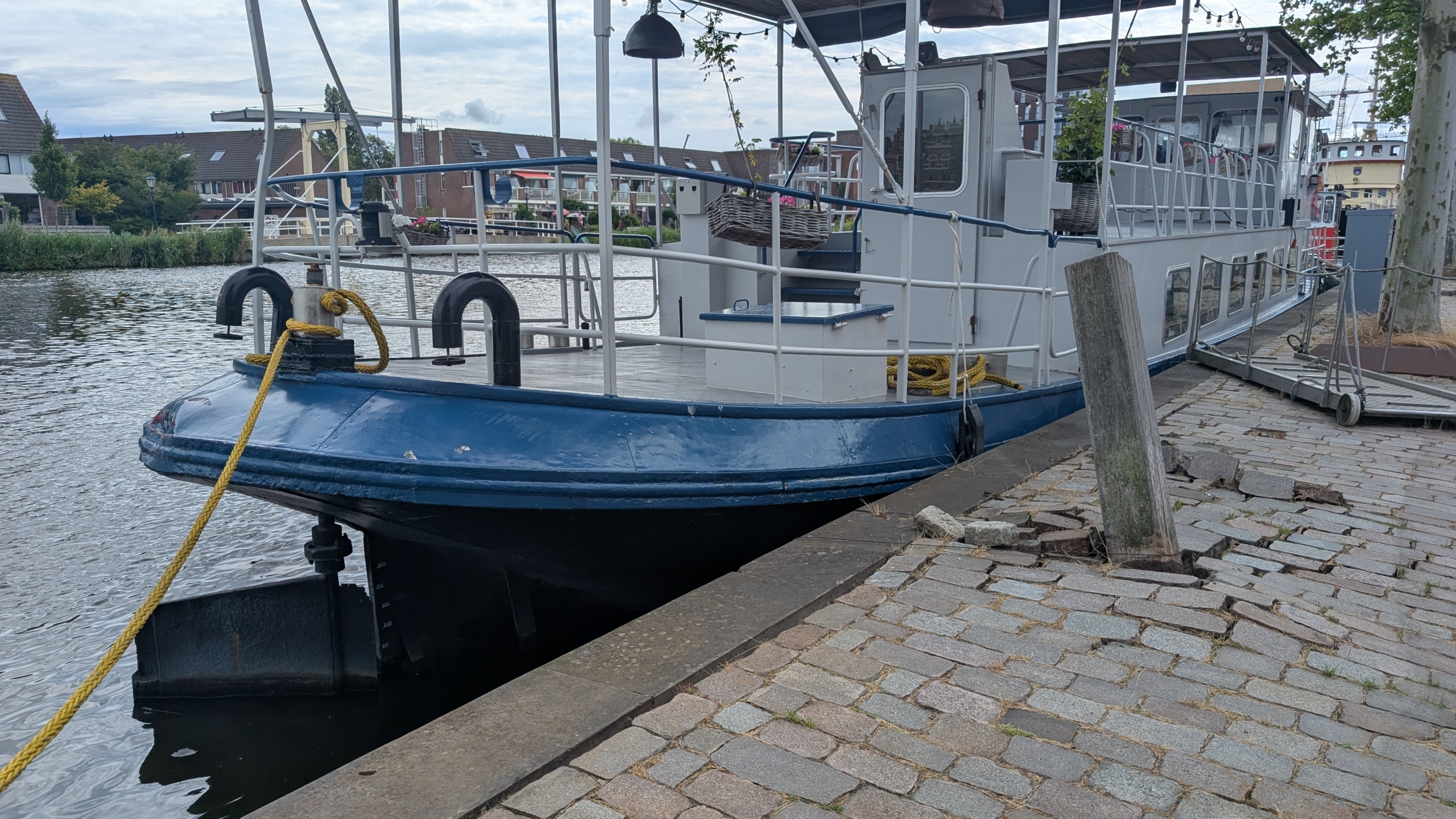 Een boot met een blauwe boeg ligt aangemeerd aan een kade met gebroken stenen.