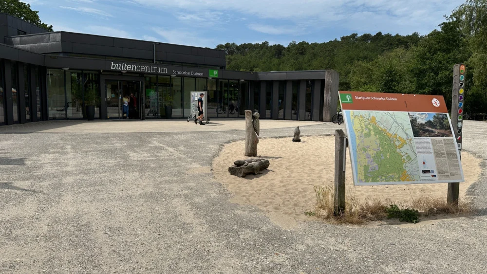 Voorkant van buitencentrum Schoorlse Duinen met informatiebord en beboste achtergrond.