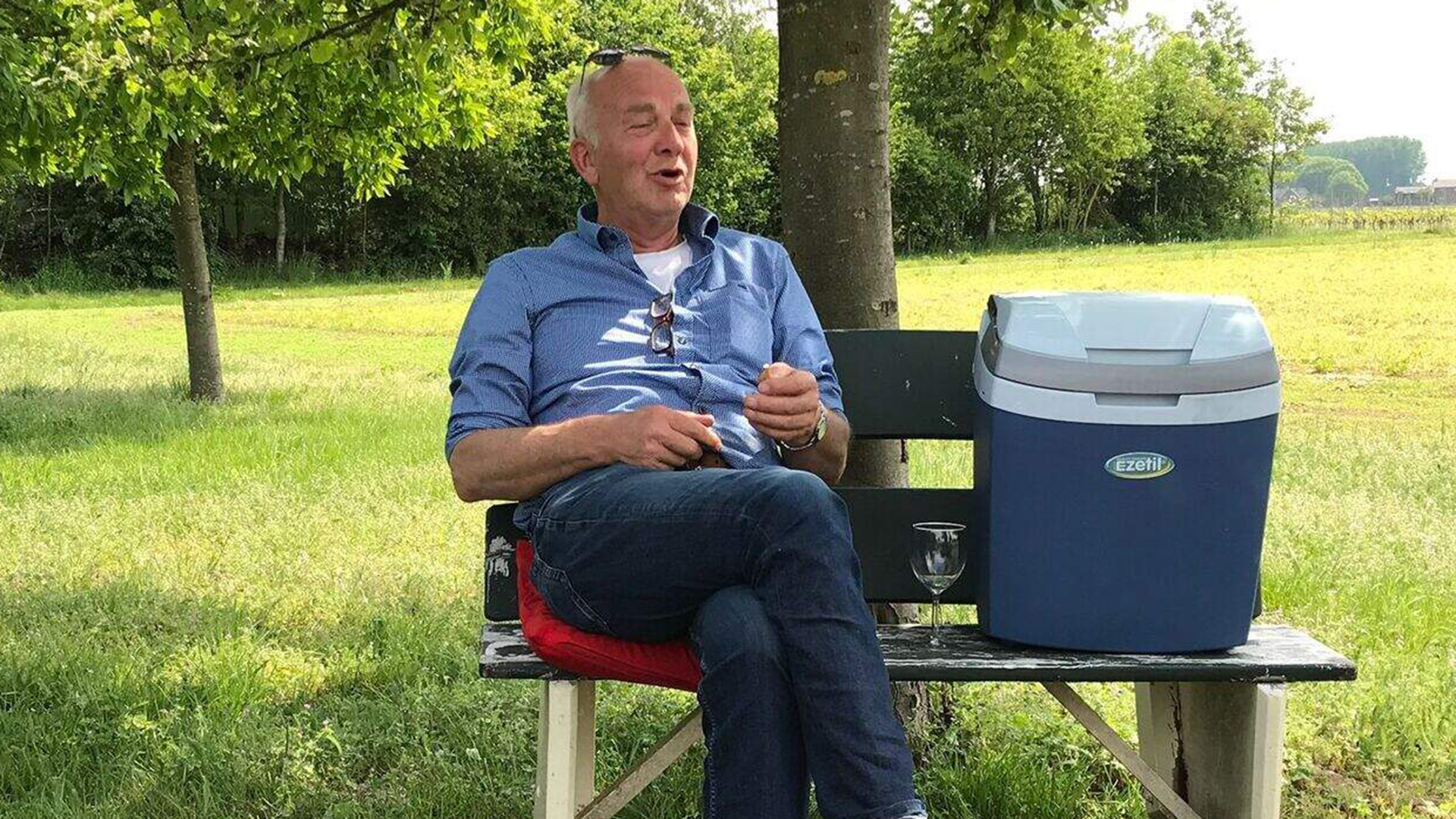 Man zit ontspannen op een bank in een groene omgeving naast een blauwe koelbox.