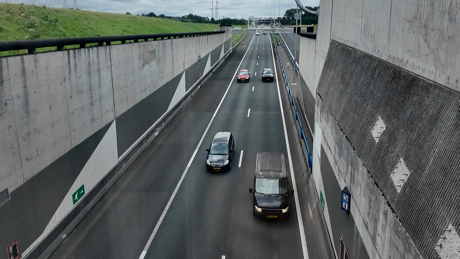 Snelweg in verdiepte ligging met meerdere auto’s tussen hoge betonnen wanden, onder een bewolkte lucht