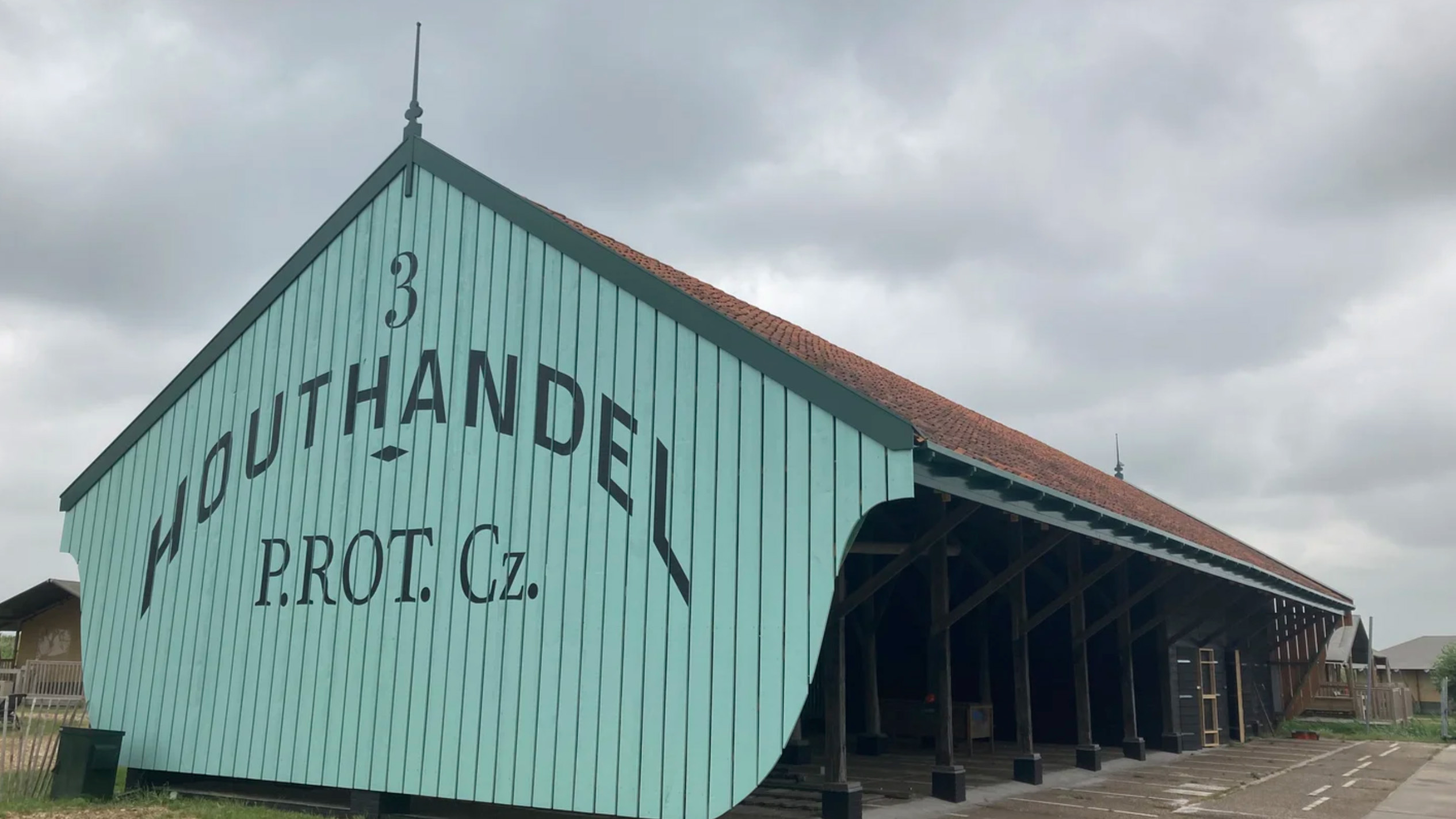 Groen houten pakhuis met rode pannenkap en grote tekst “Houthandel P. ROT. Cz.” op de gevel
